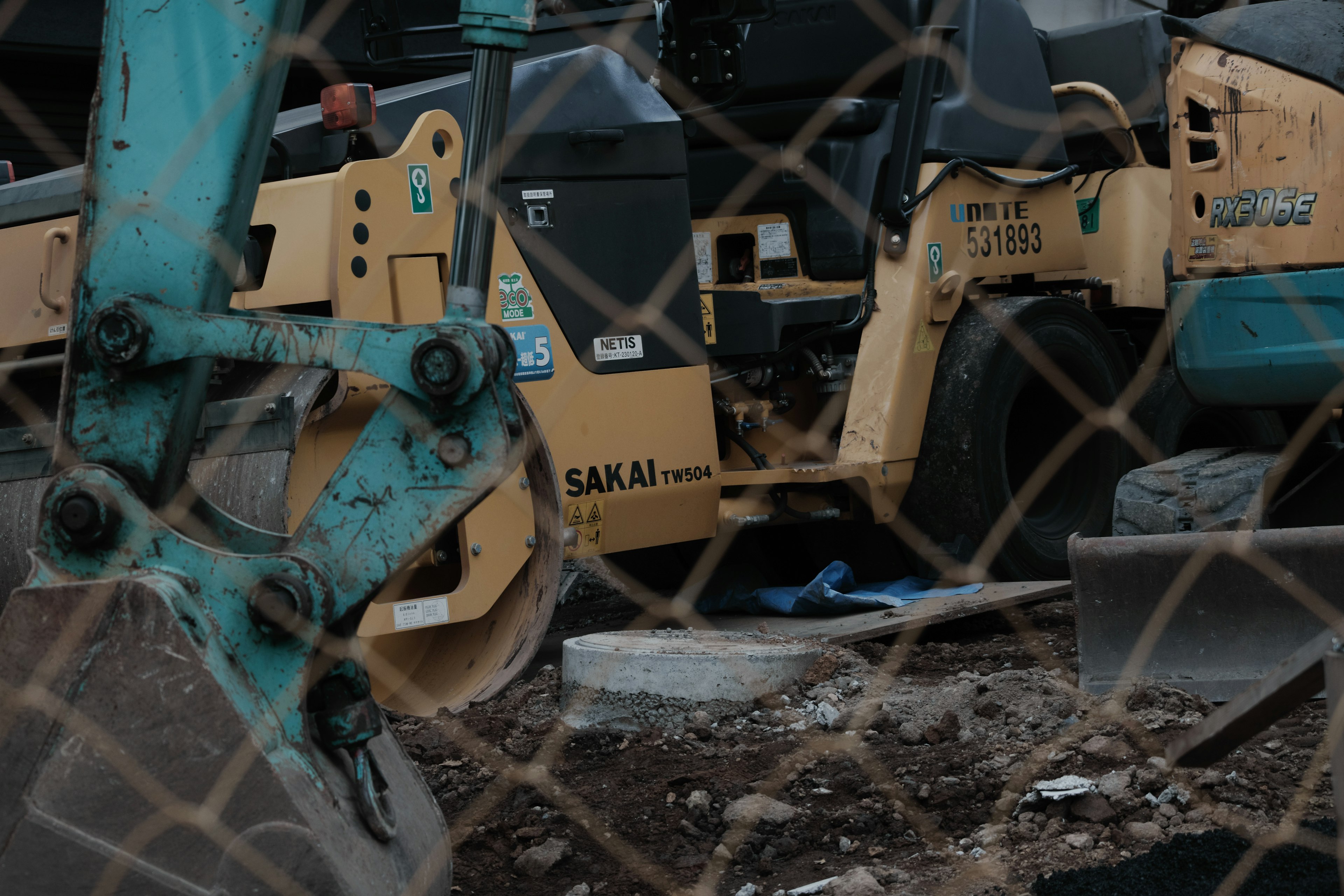Partie d'un véhicule de construction vue à travers une clôture avec de la terre environnante