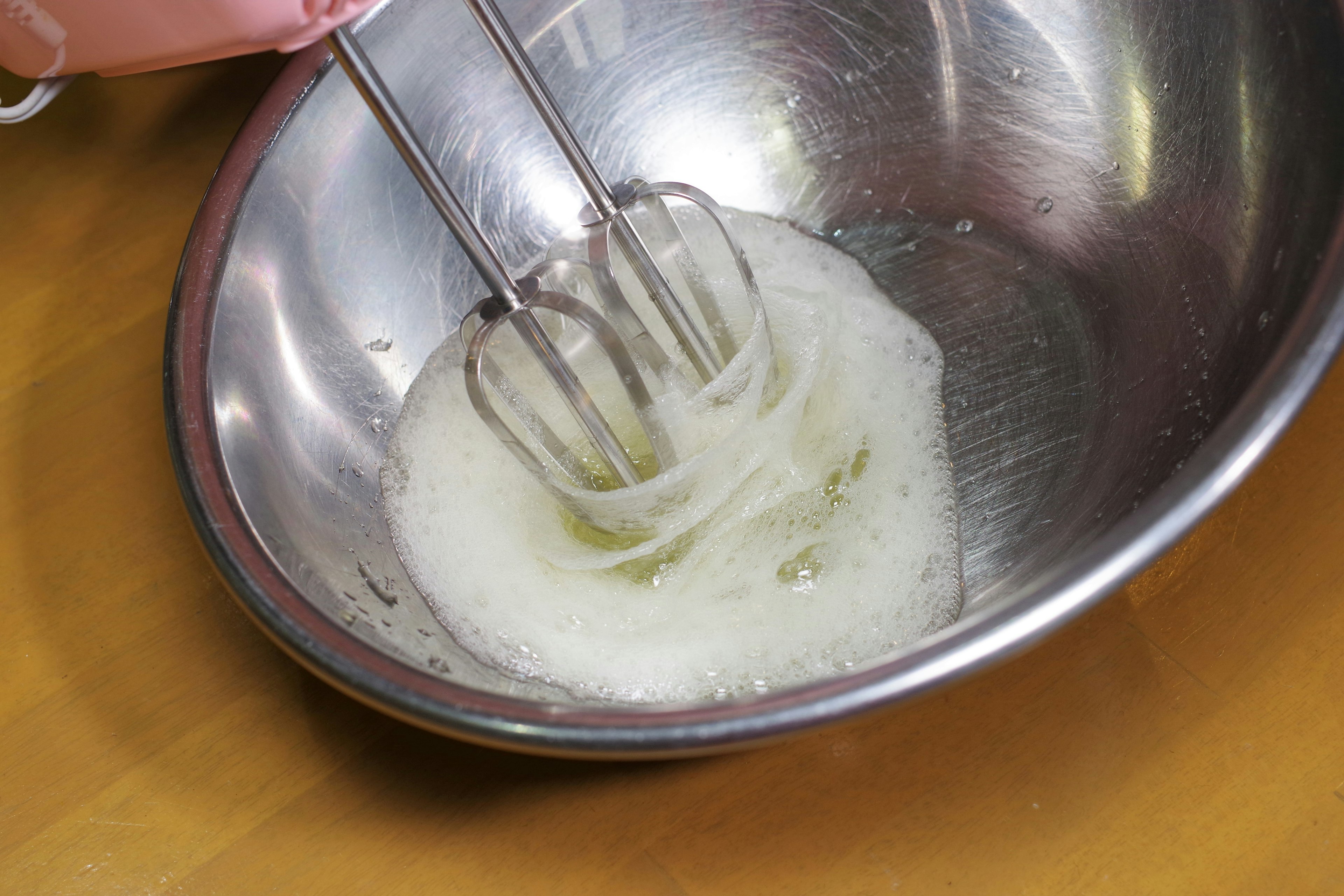 Primer plano de una batidora de mano batiendo claras de huevo en un bol de metal