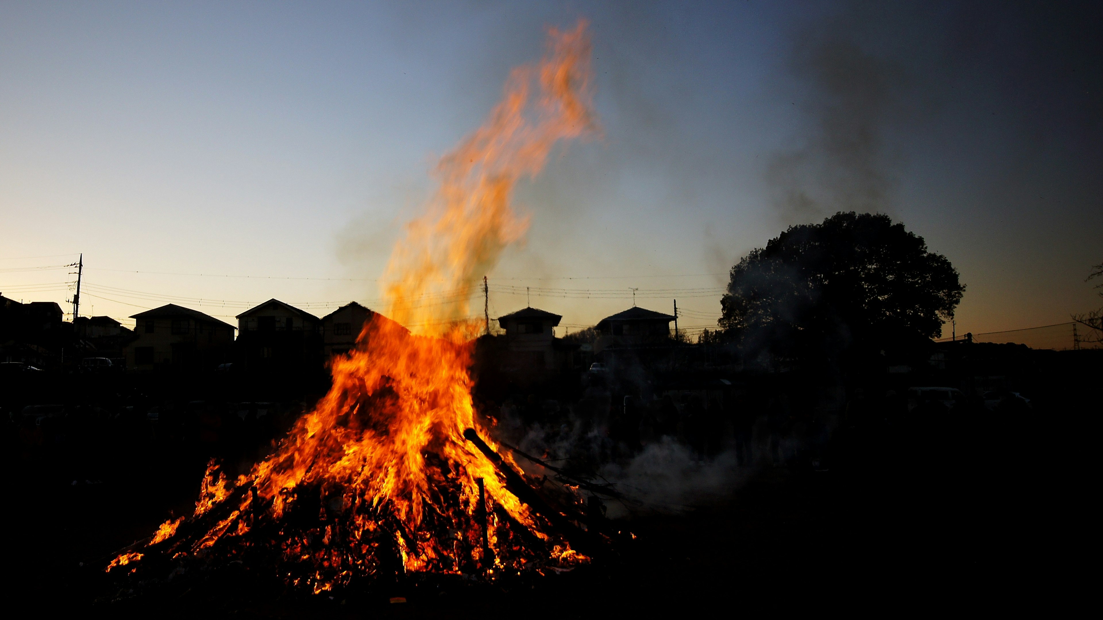 Ein großes Lagerfeuer mit aufsteigenden Flammen während des Sonnenuntergangs und silhouettierten Häusern