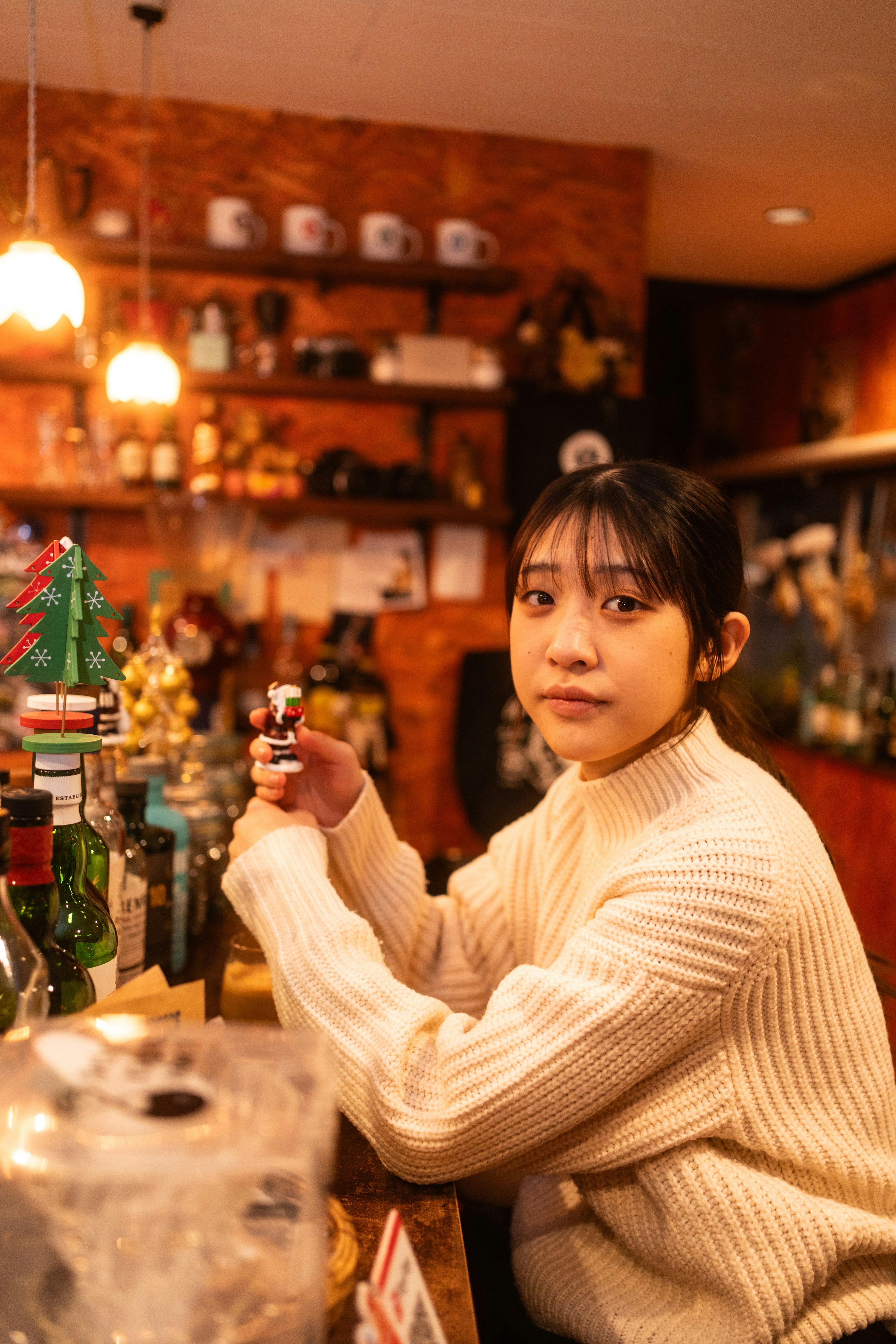 Eine Frau sitzt am Tresen und hält ein Getränk mit Bar-Dekor und Flaschen im Hintergrund