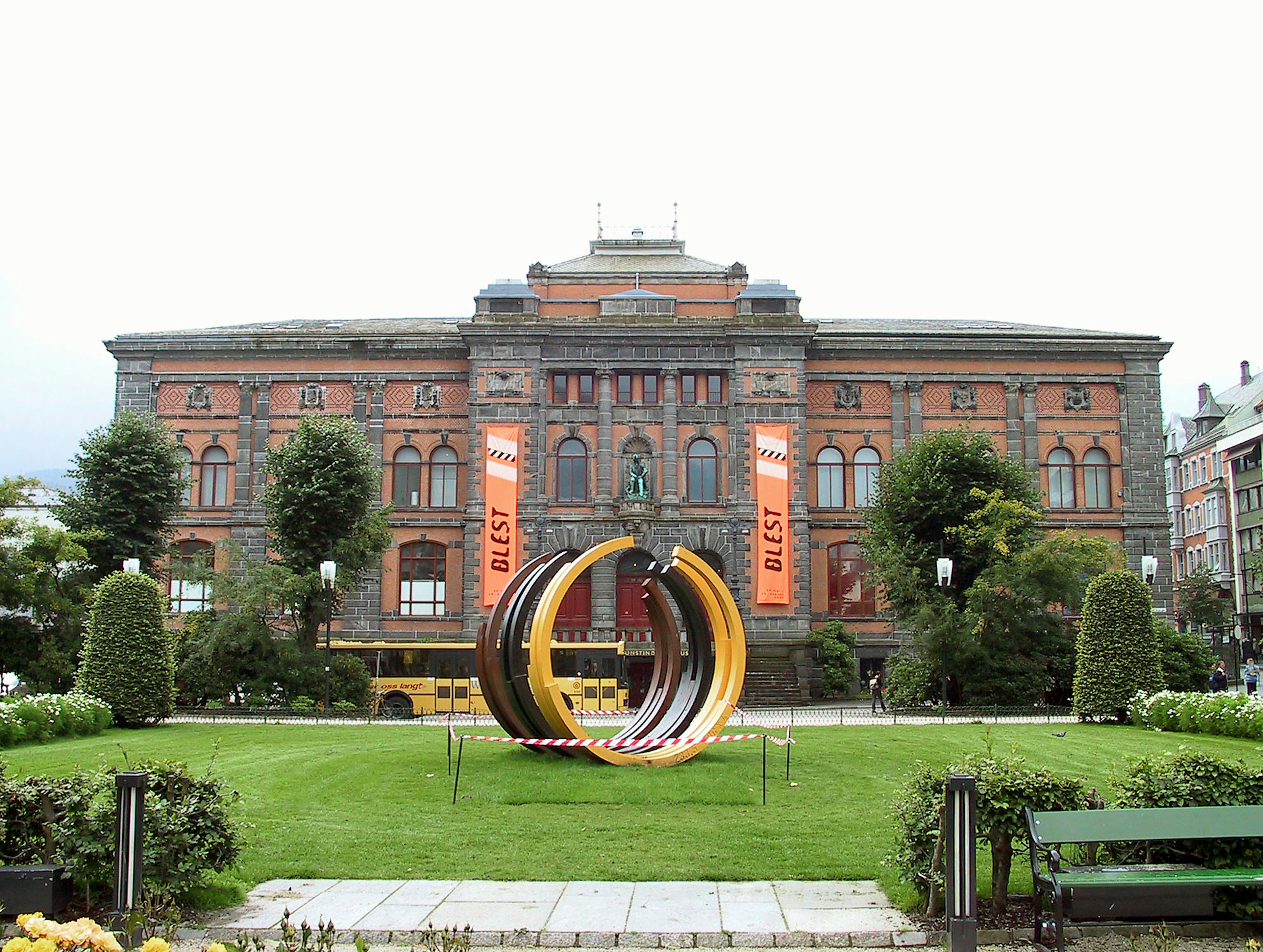 Edificio histórico de ladrillo rojo con escultura moderna en un parque exuberante