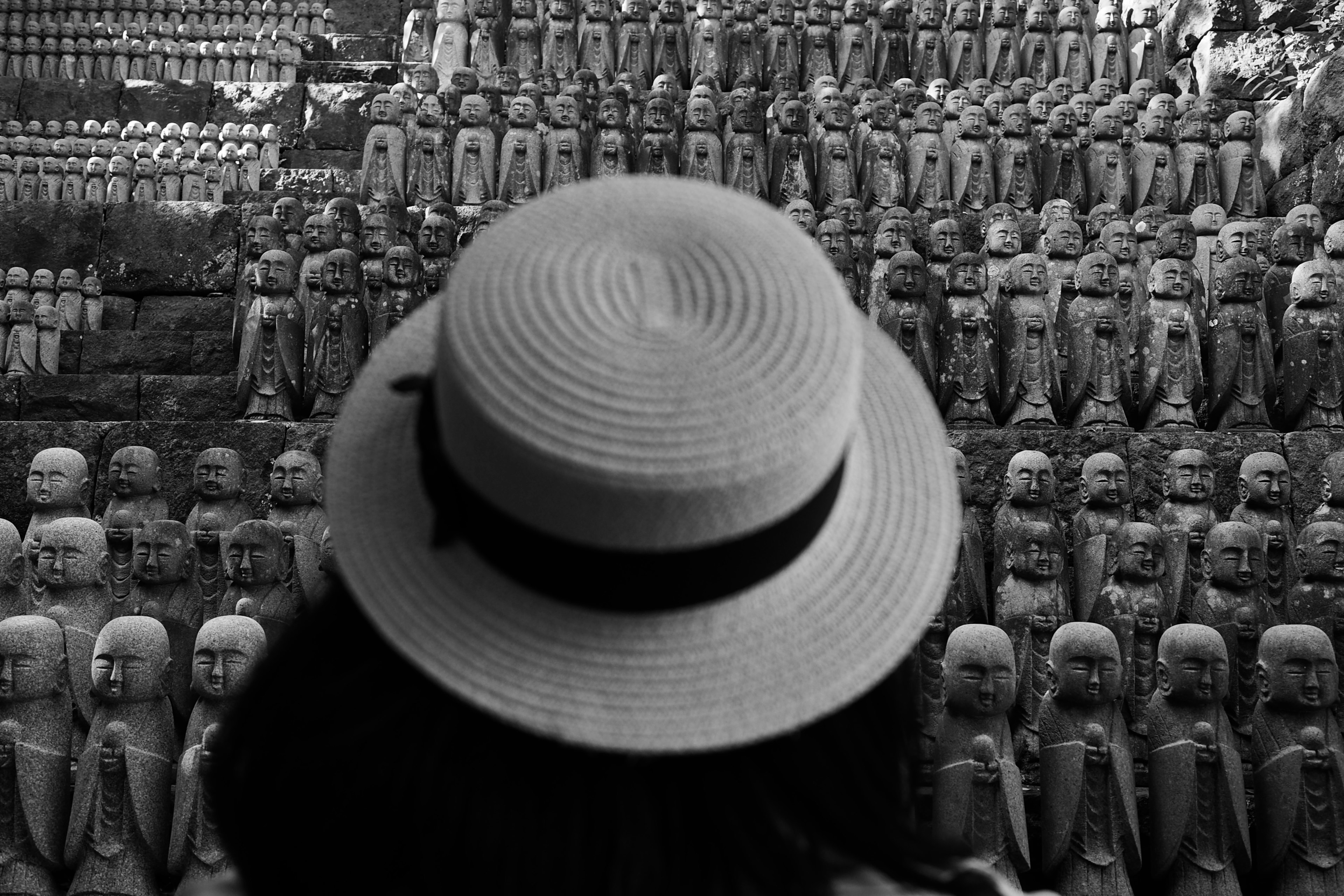 Persona con cappello che osserva numerose statue di pietra in un contesto monocromatico