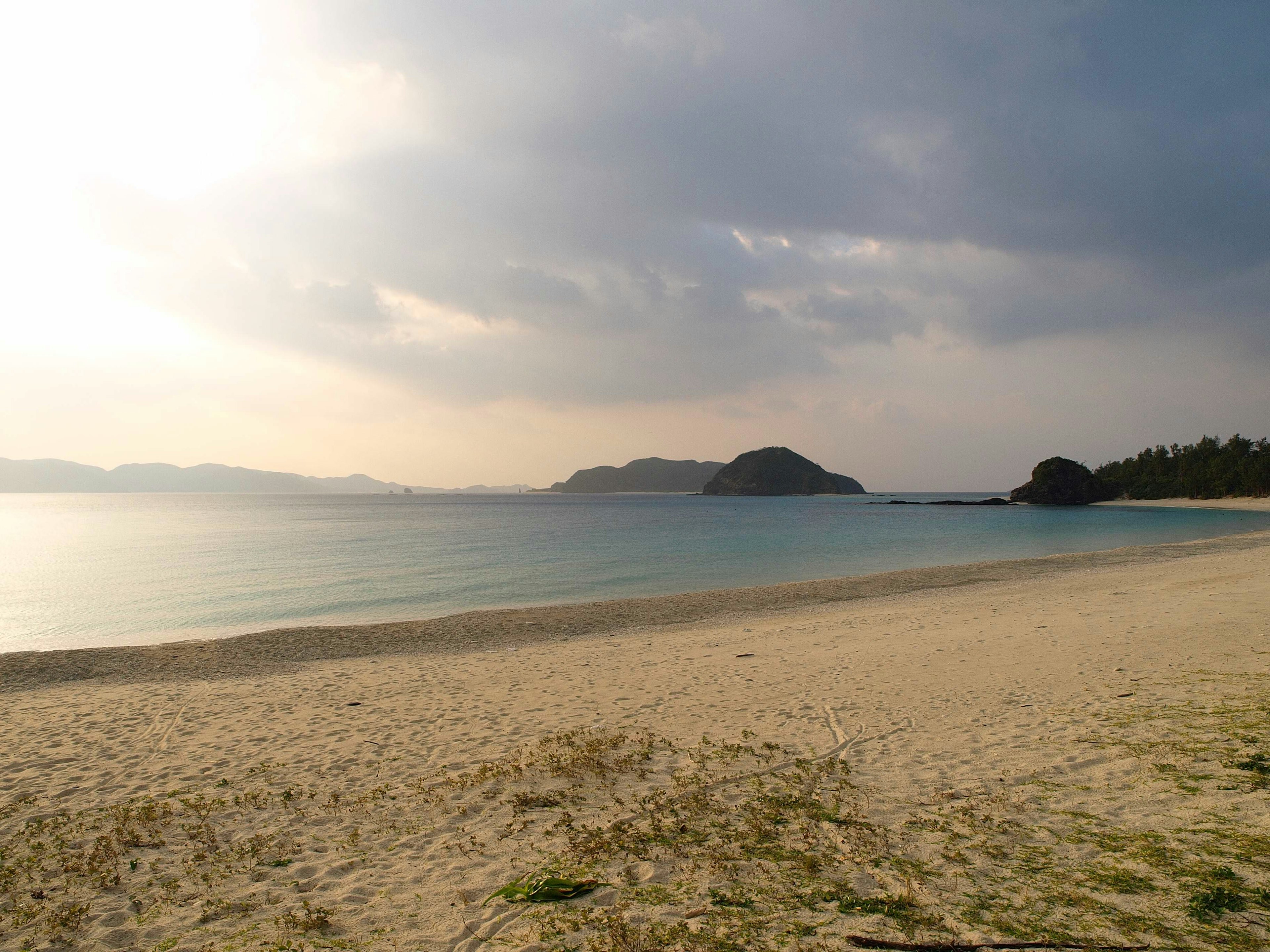 Paisaje de mar tranquilo y playa de arena con cielo nublado y una isla lejana