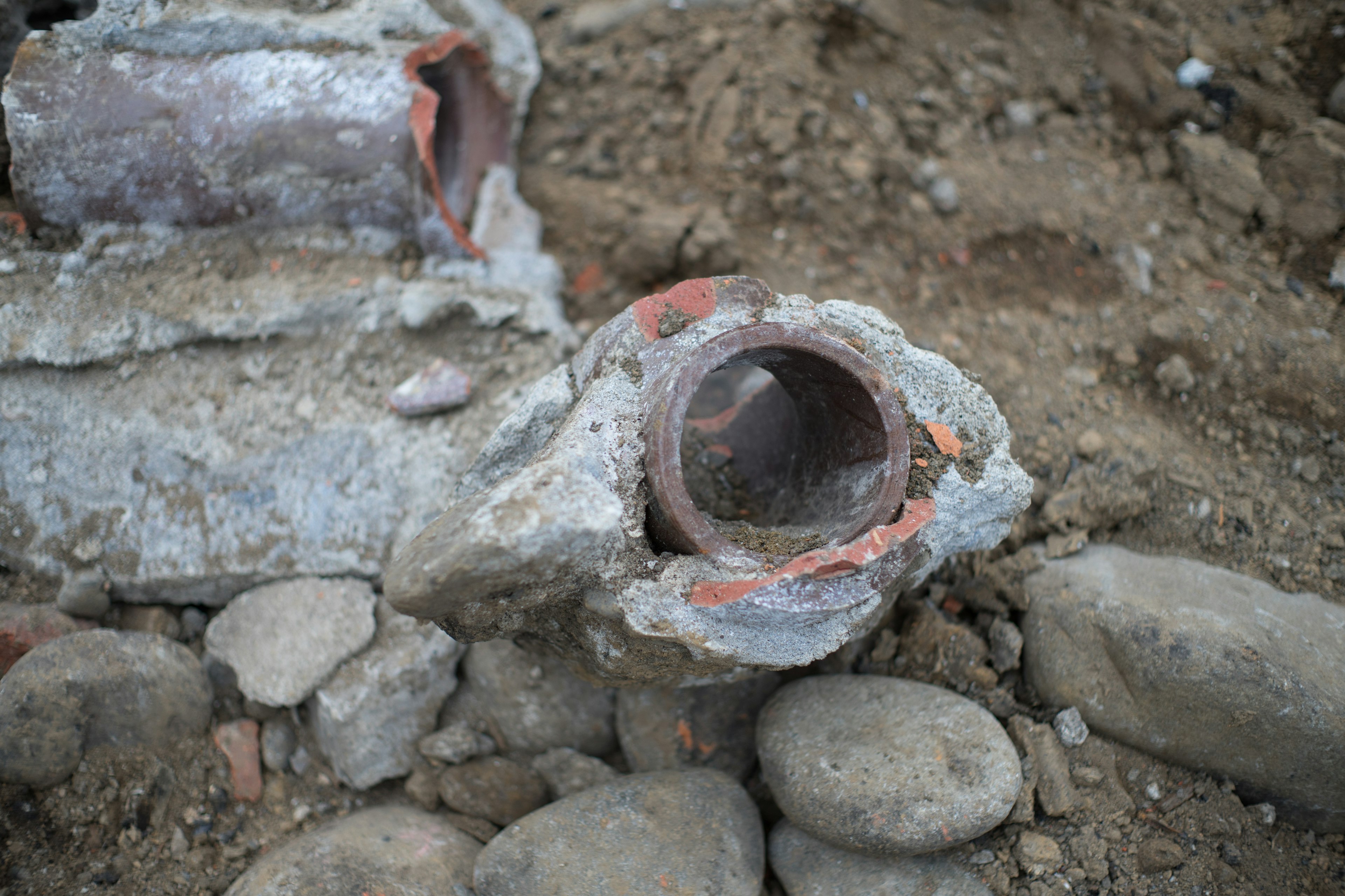 Fragmento de tubería antigua parcialmente enterrado en el suelo piezas de ladrillo rojo visibles