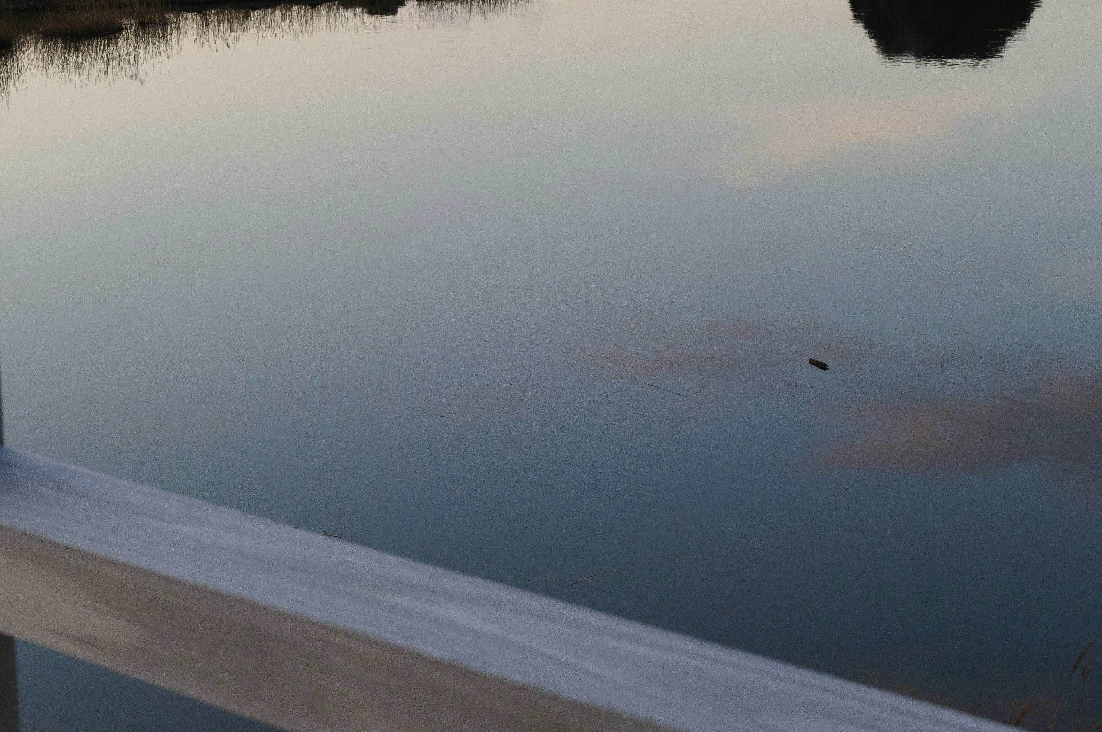 Superficie tranquila del lago reflejando el paisaje con una barandilla blanca