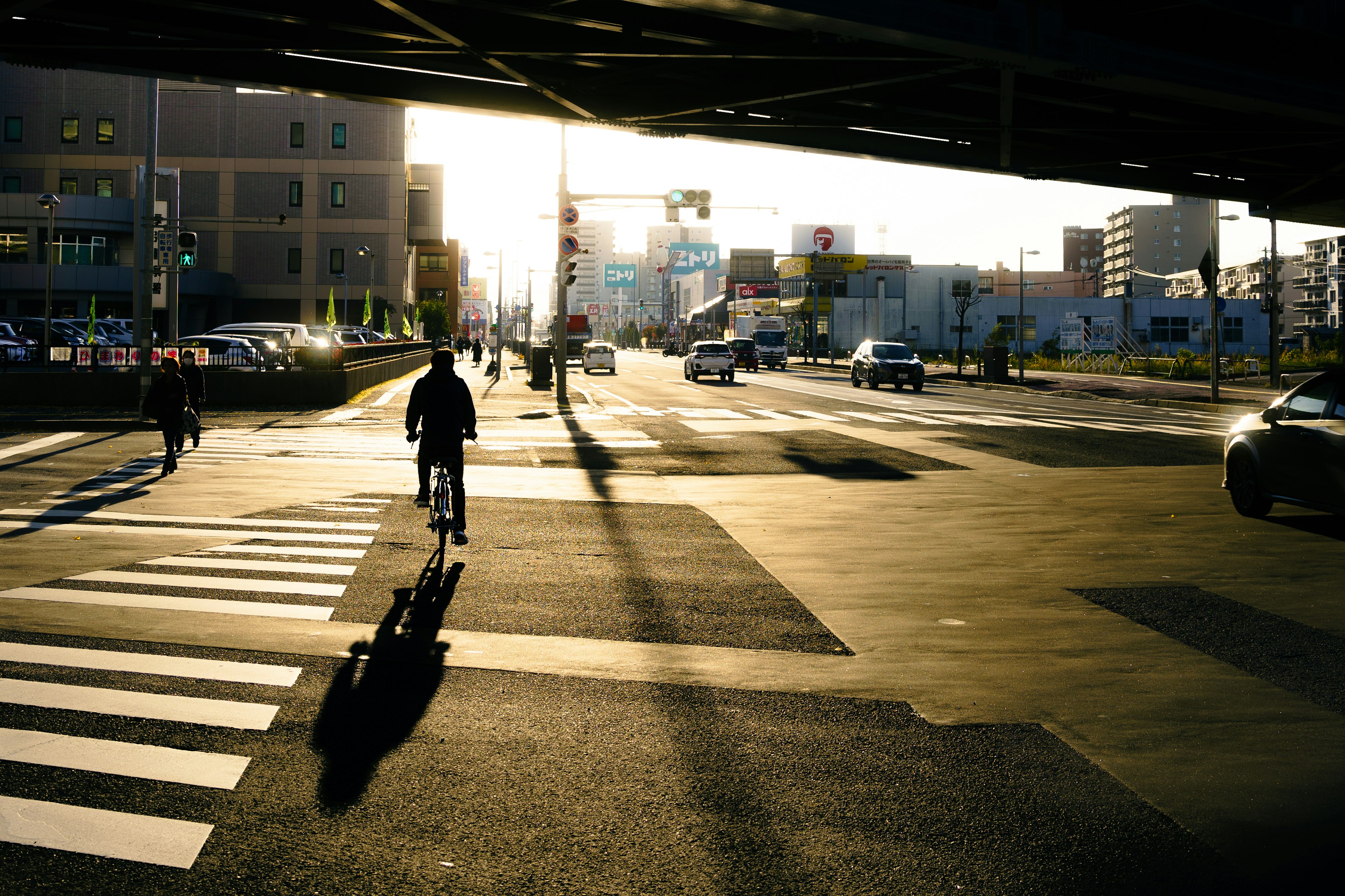 Silhouette di un ciclista e pedoni a un attraversamento pedonale al tramonto