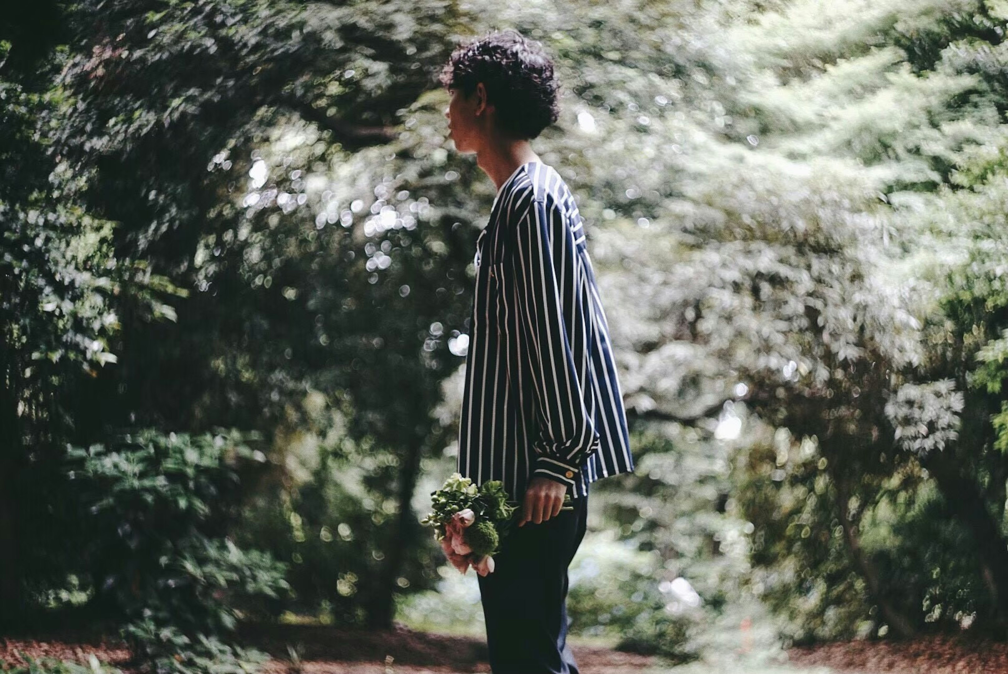 Person wearing a striped shirt standing in a green forest