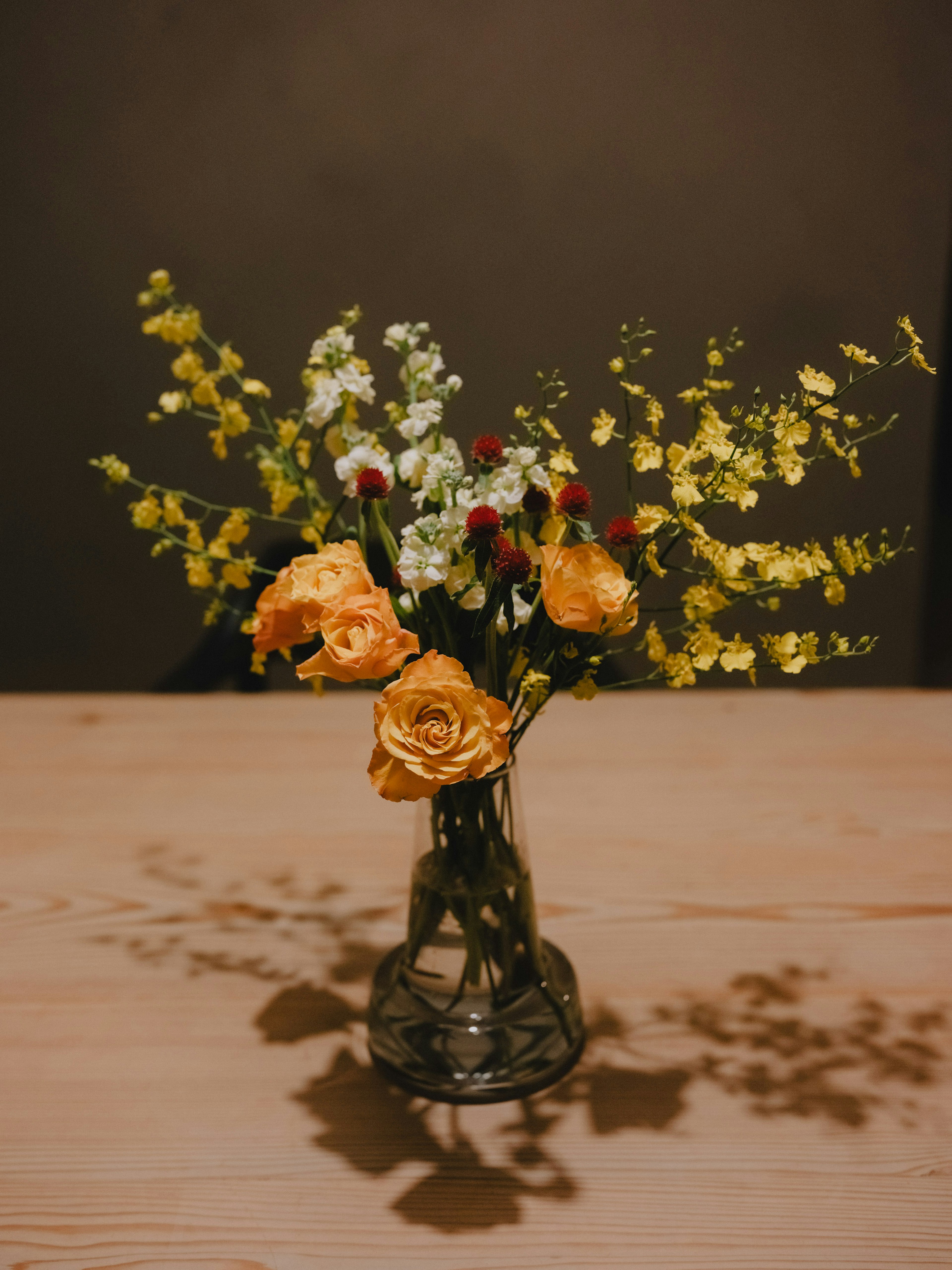 Un ramo de rosas amarillas y flores blancas en un jarrón de vidrio