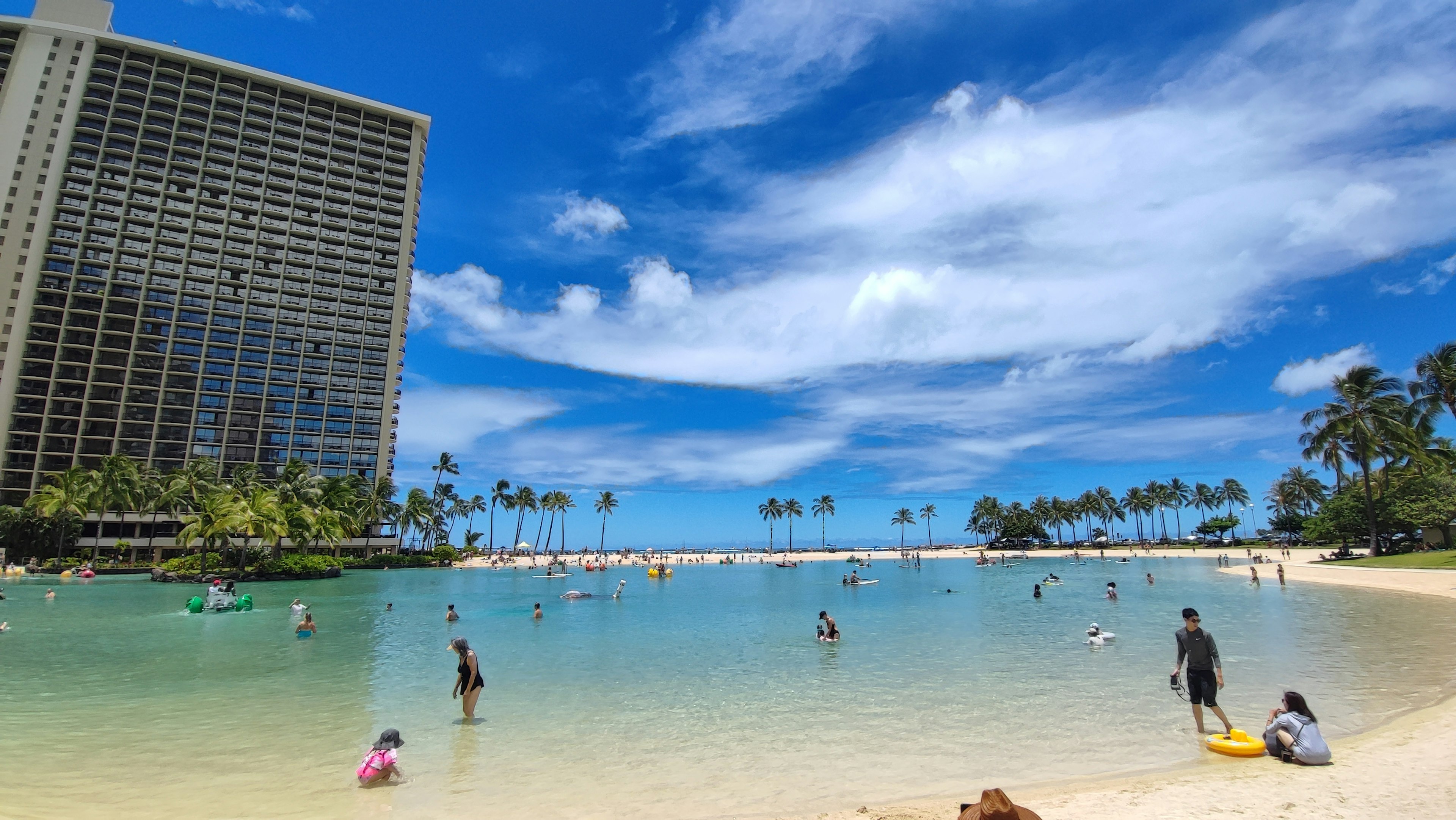 Orang-orang menikmati pantai dan air di bawah langit biru cerah di Honolulu