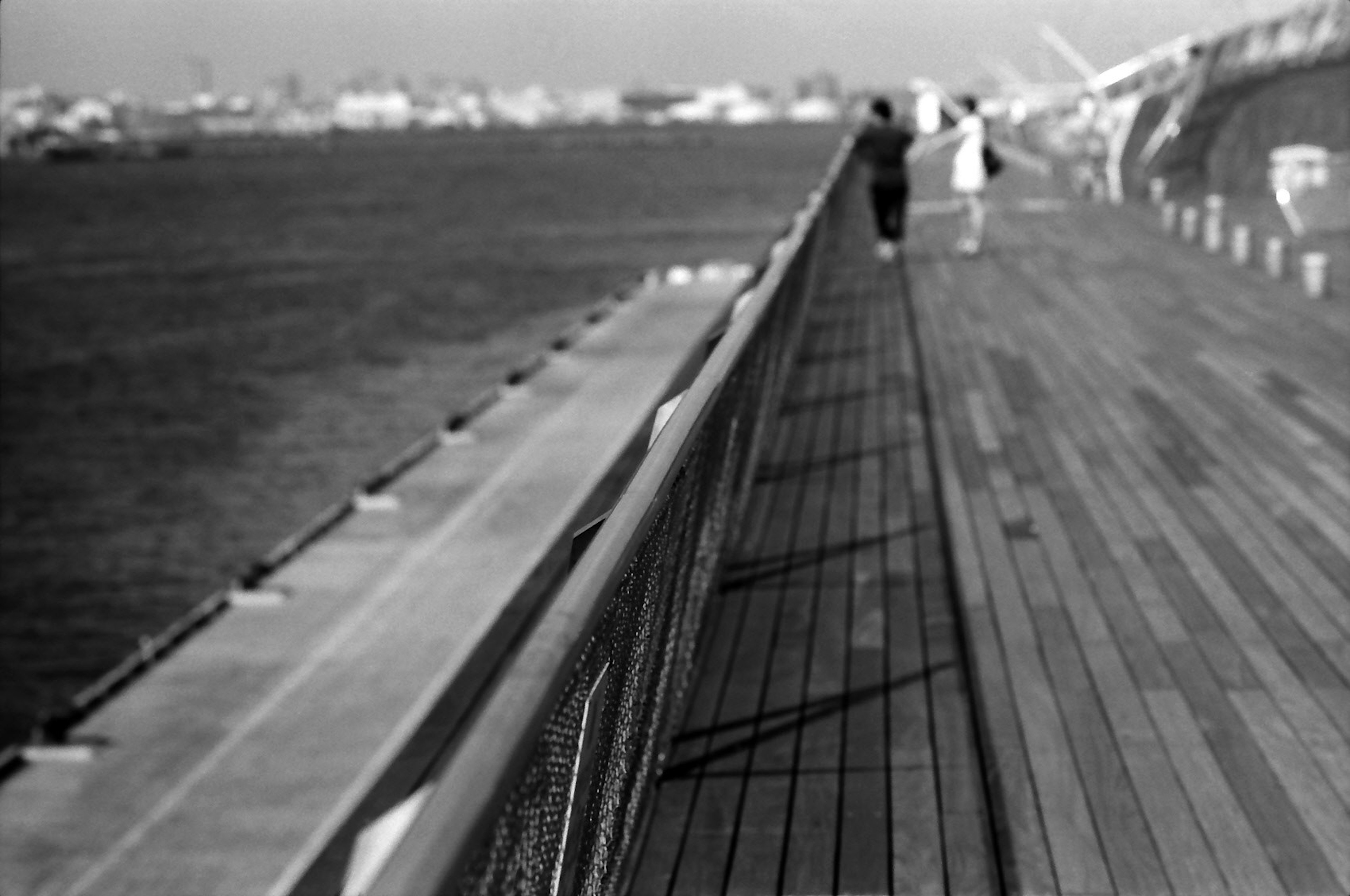 Black and white image of a seaside pier with people walking