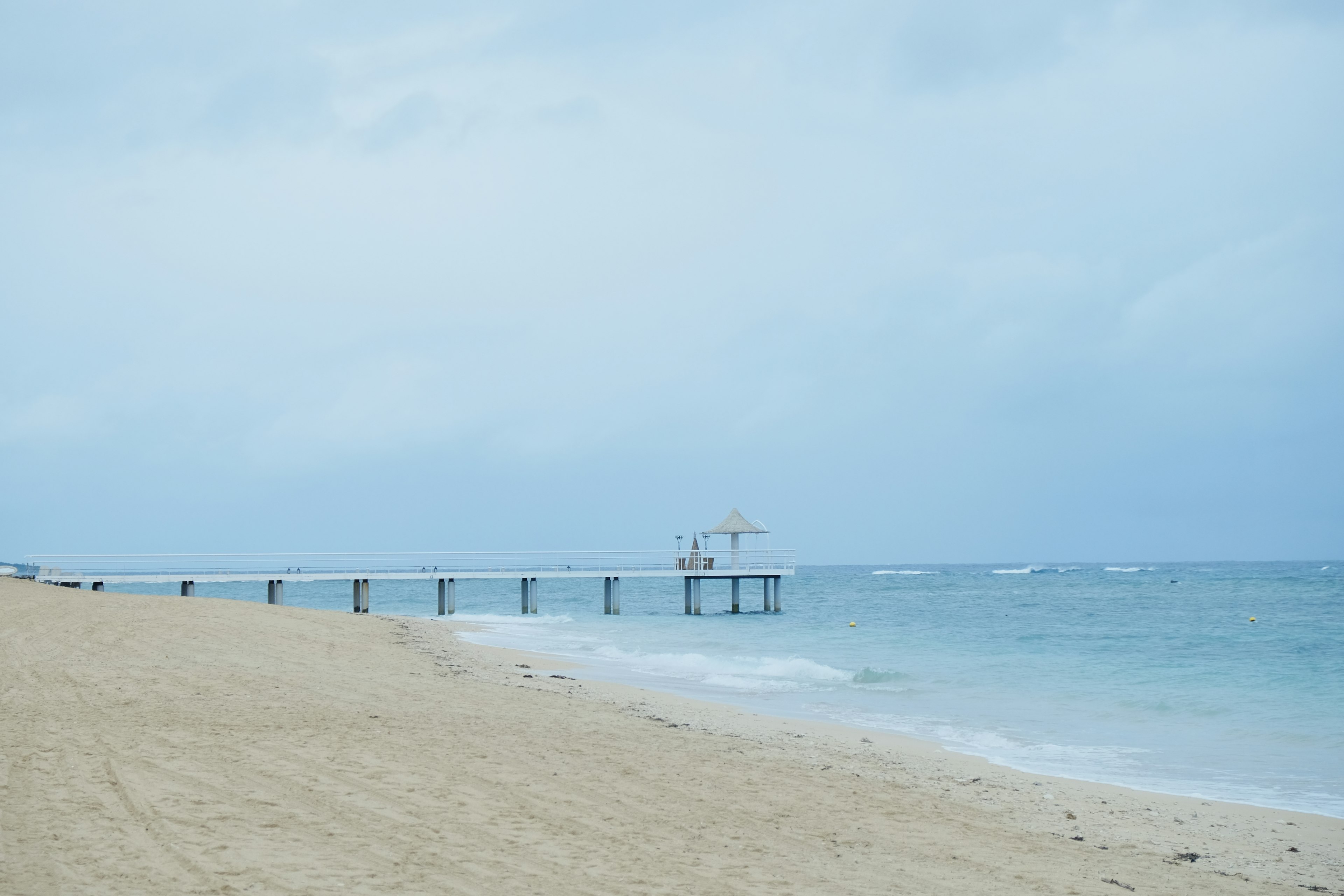 Pemandangan pantai yang tenang dengan laut biru dan dermaga yang membentang ke dalam air