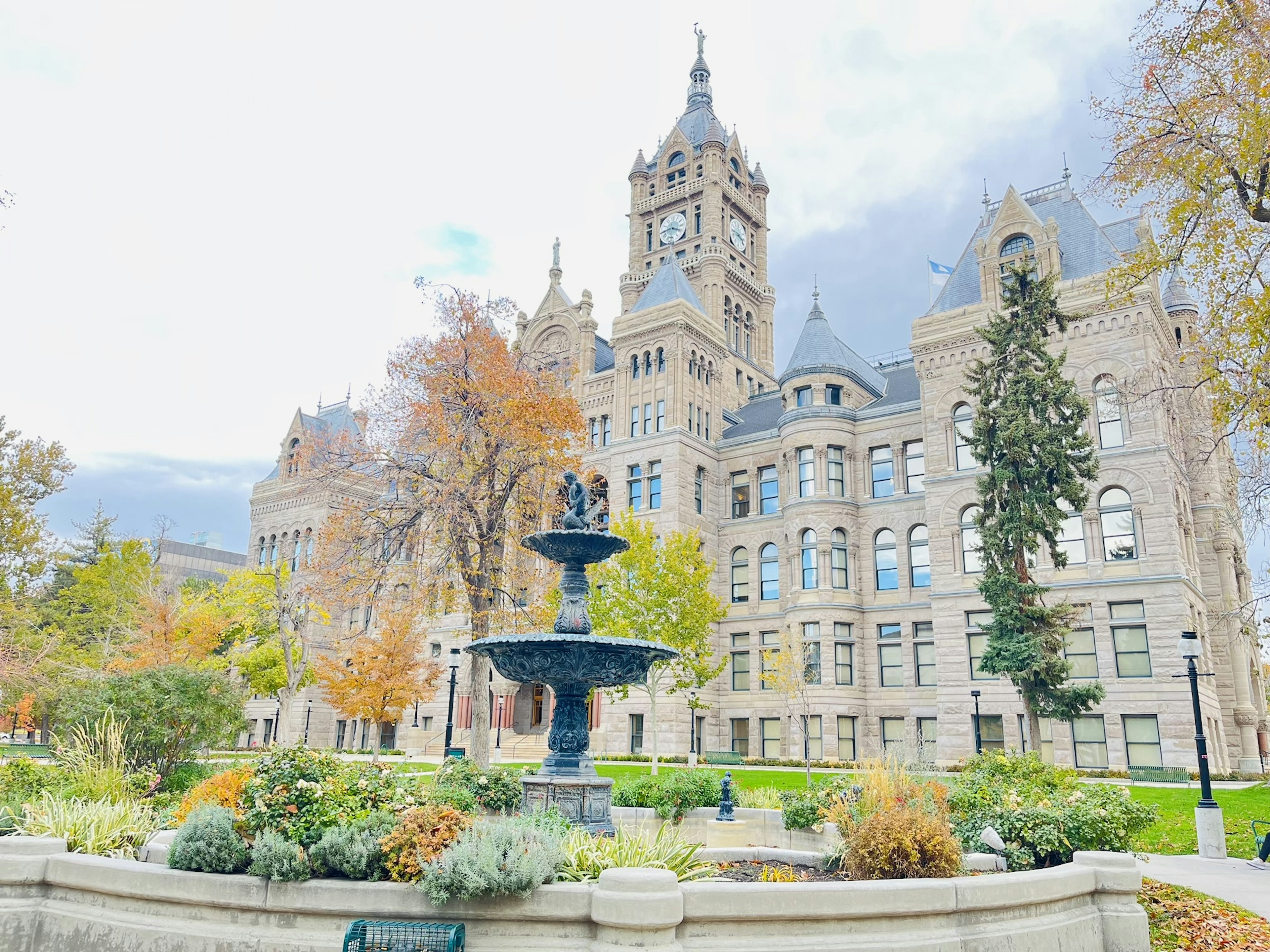 Brunnen in einem Park mit herbstlichem Laub und historischem Gebäude im Hintergrund