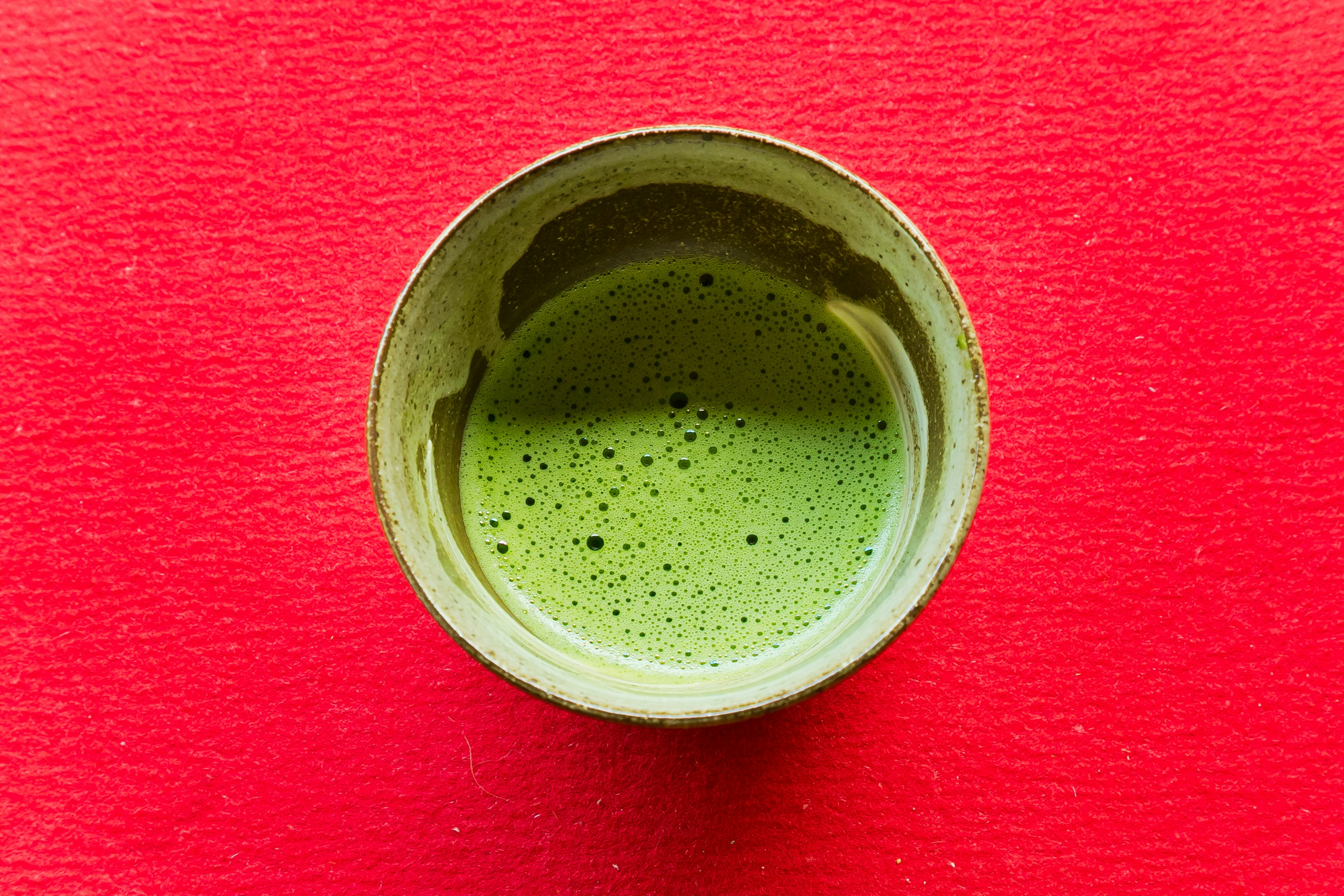 Green matcha tea in a bowl on a red background