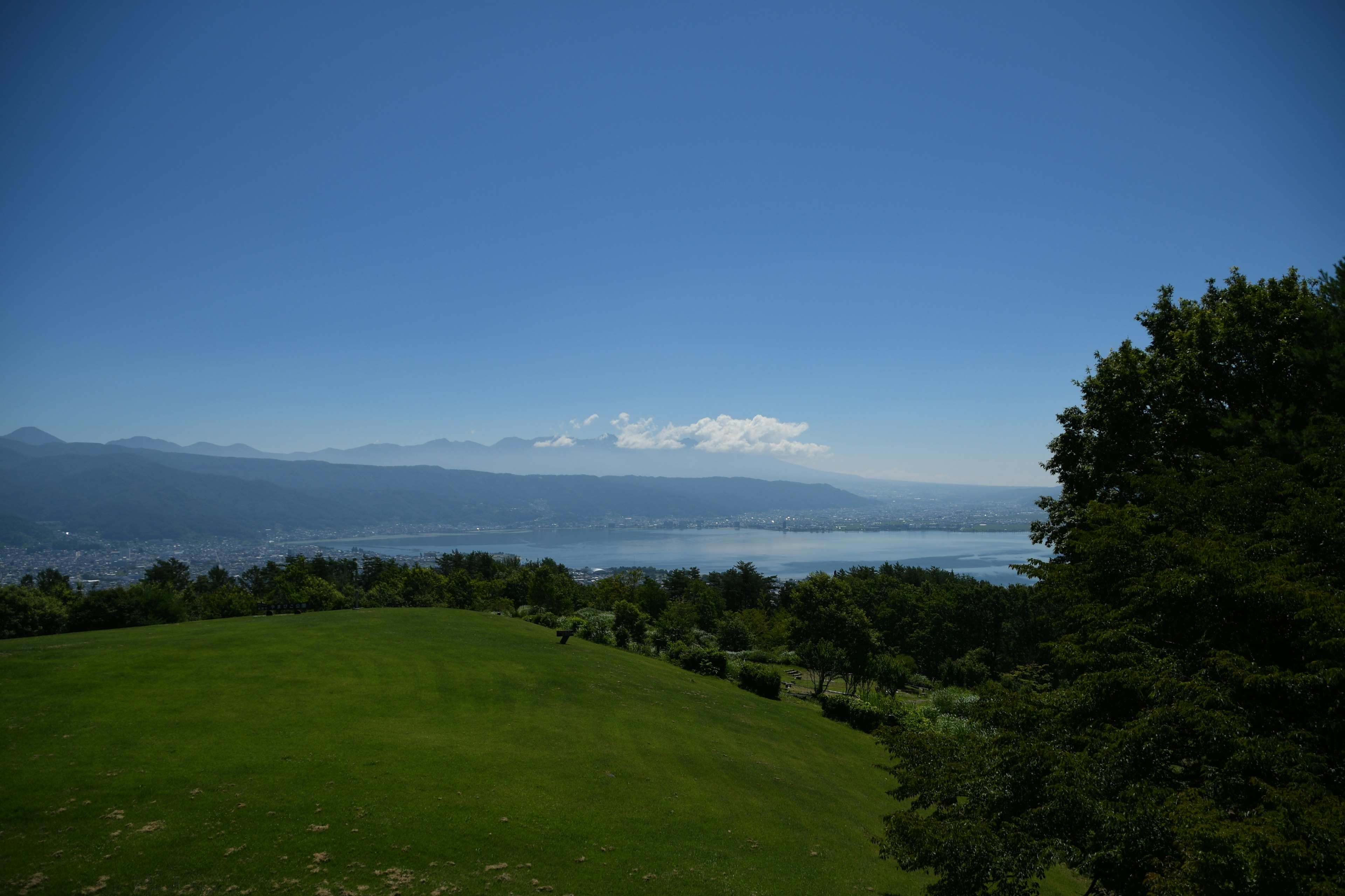 青空と緑の草原が広がる風景　遠くに山と湖が見える