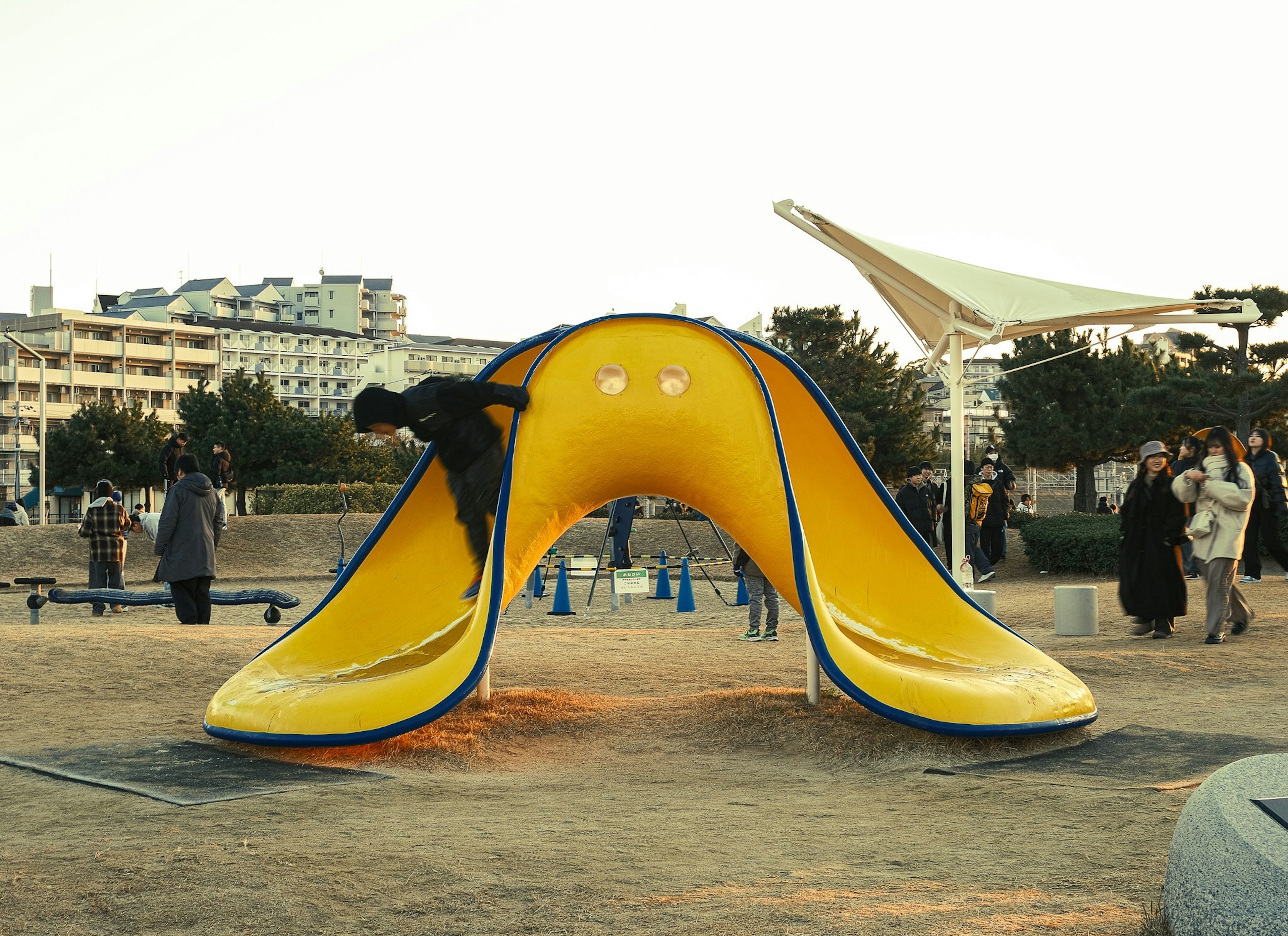 Niños jugando en un tobogán amarillo en un parque con espectadores cerca