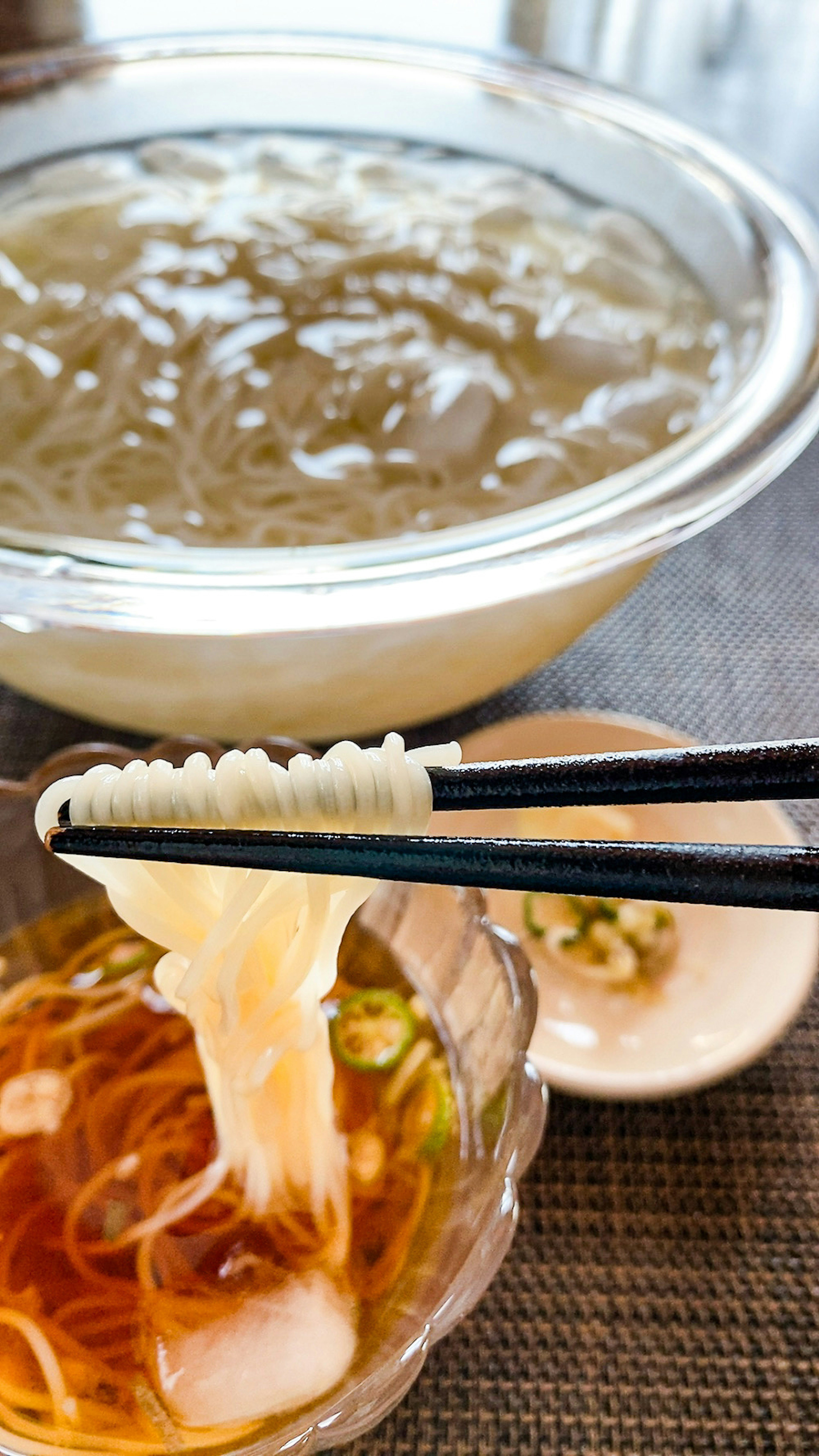 A photo of thin noodles being lifted from a clear broth with chopsticks