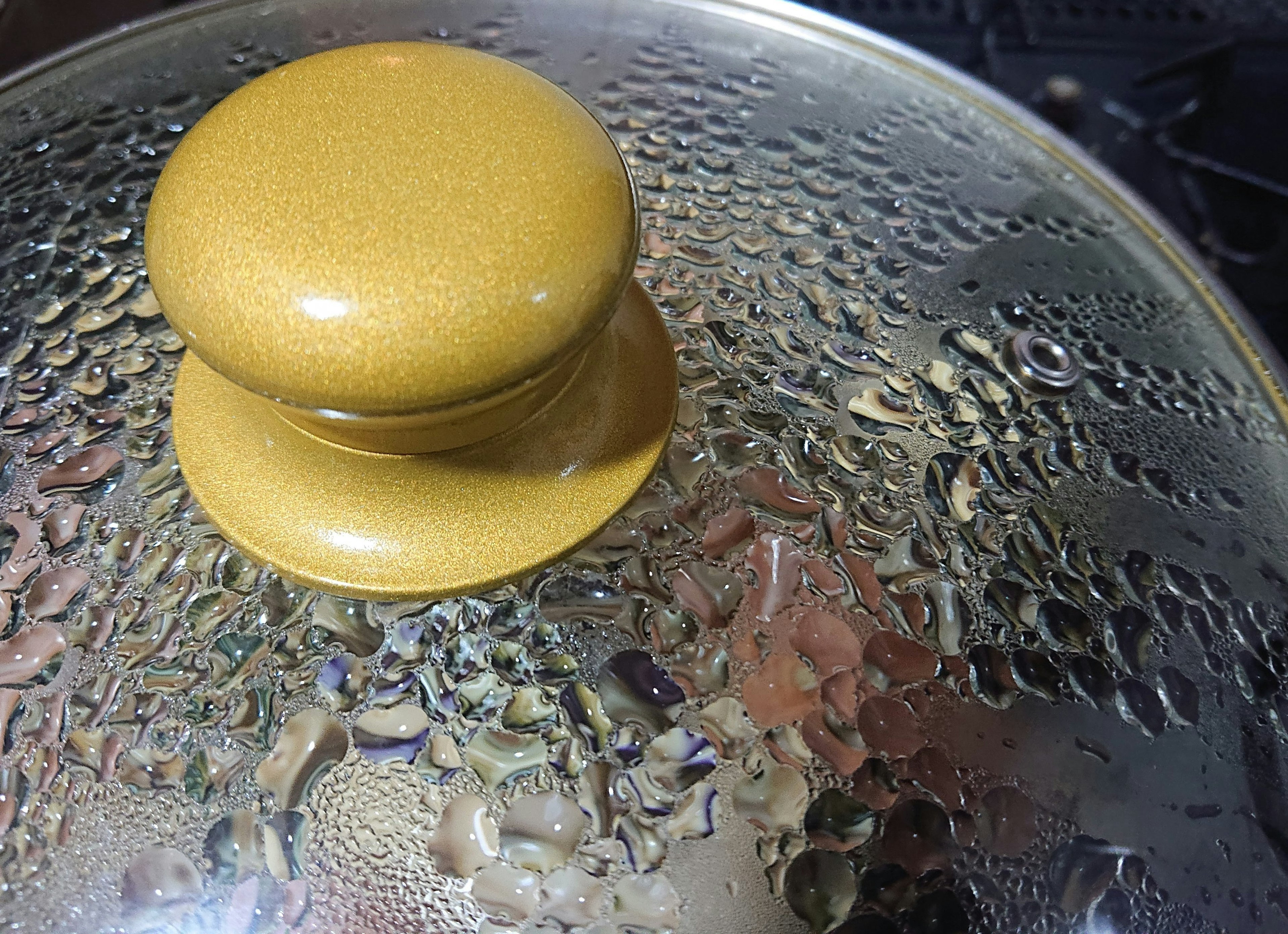 Close-up of a pot lid with a yellow knob and condensation droplets