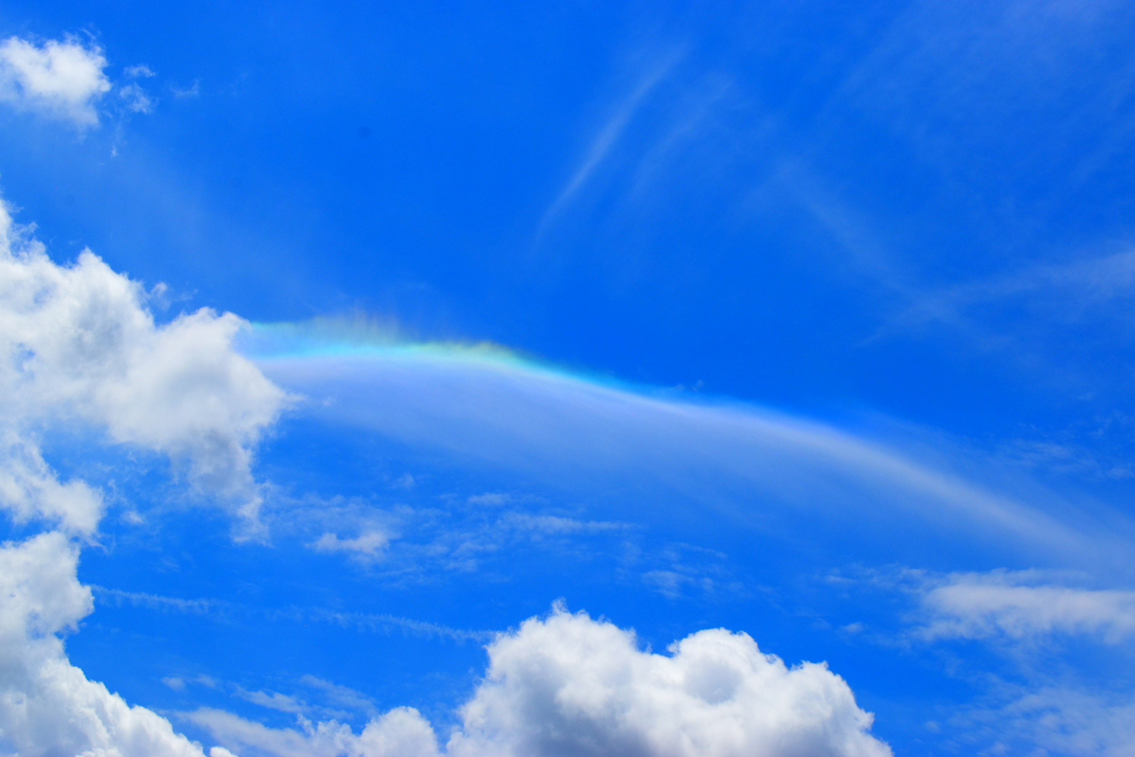 A faint rainbow appearing between blue sky and white clouds