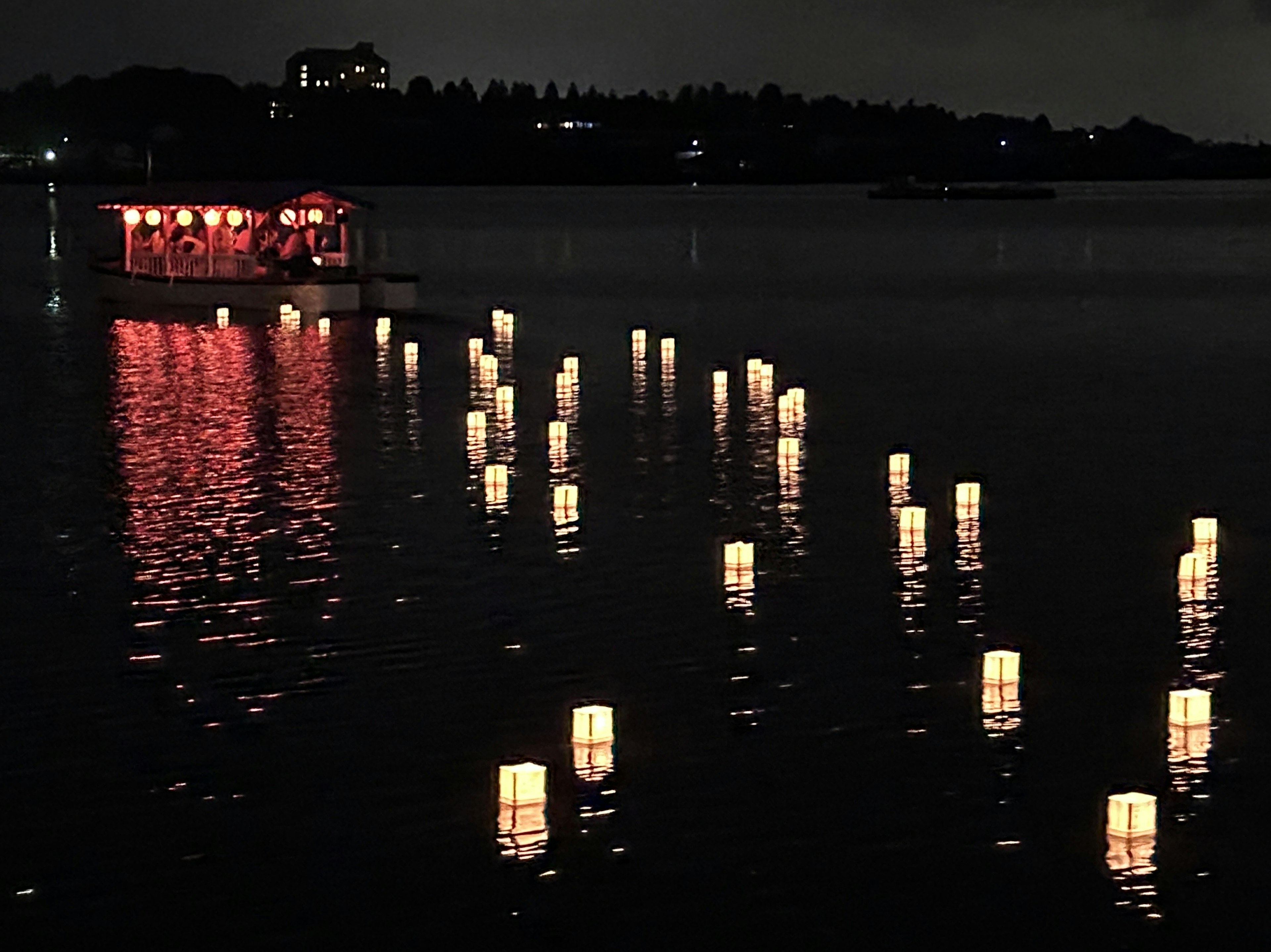 Linternas flotando en un lago de noche con un pequeño bote iluminado en rojo