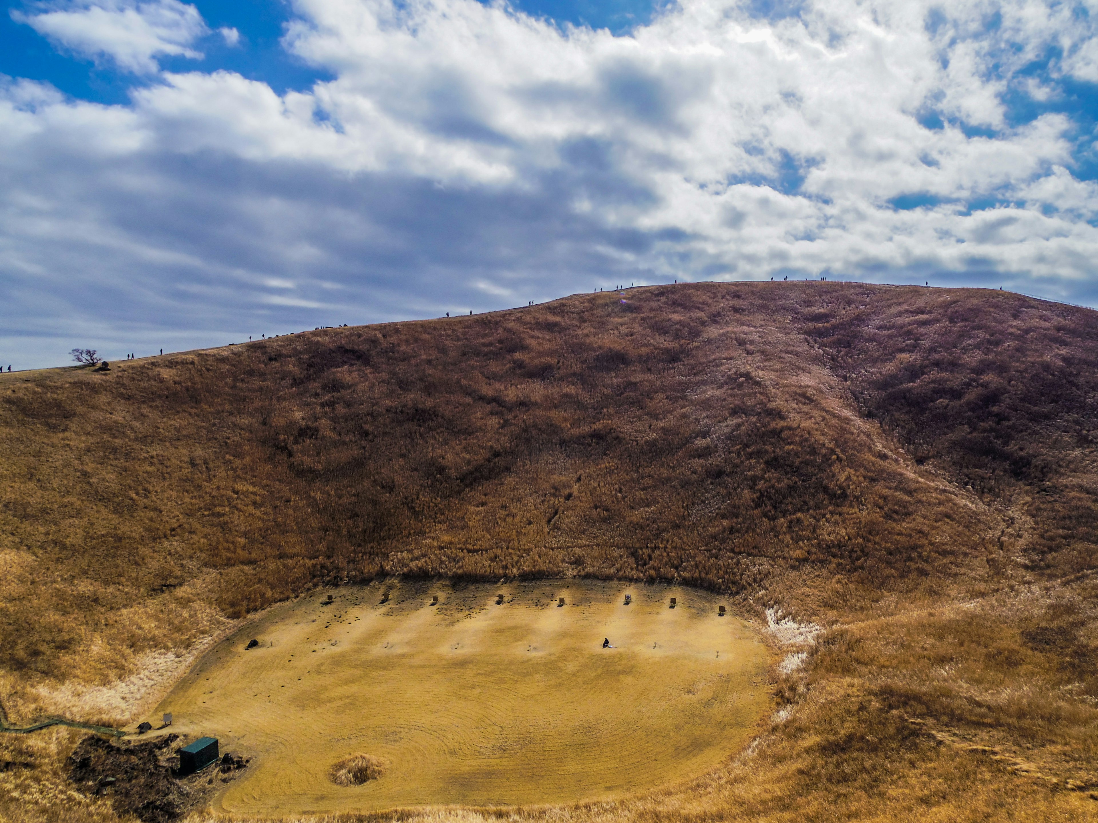 Open field surrounded by dry hills and a blue sky with clouds