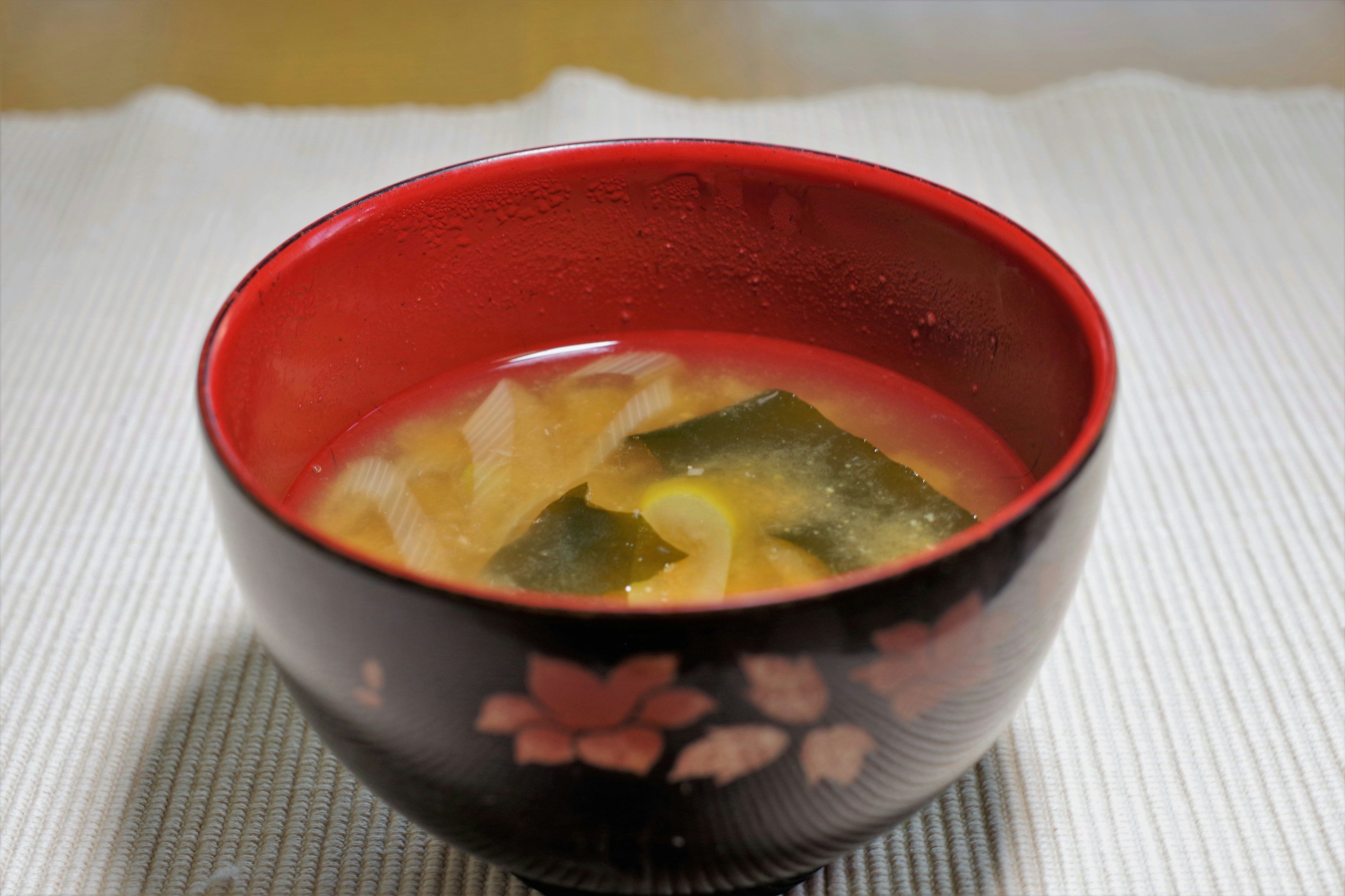 Miso soup served in a red bowl with visible ingredients