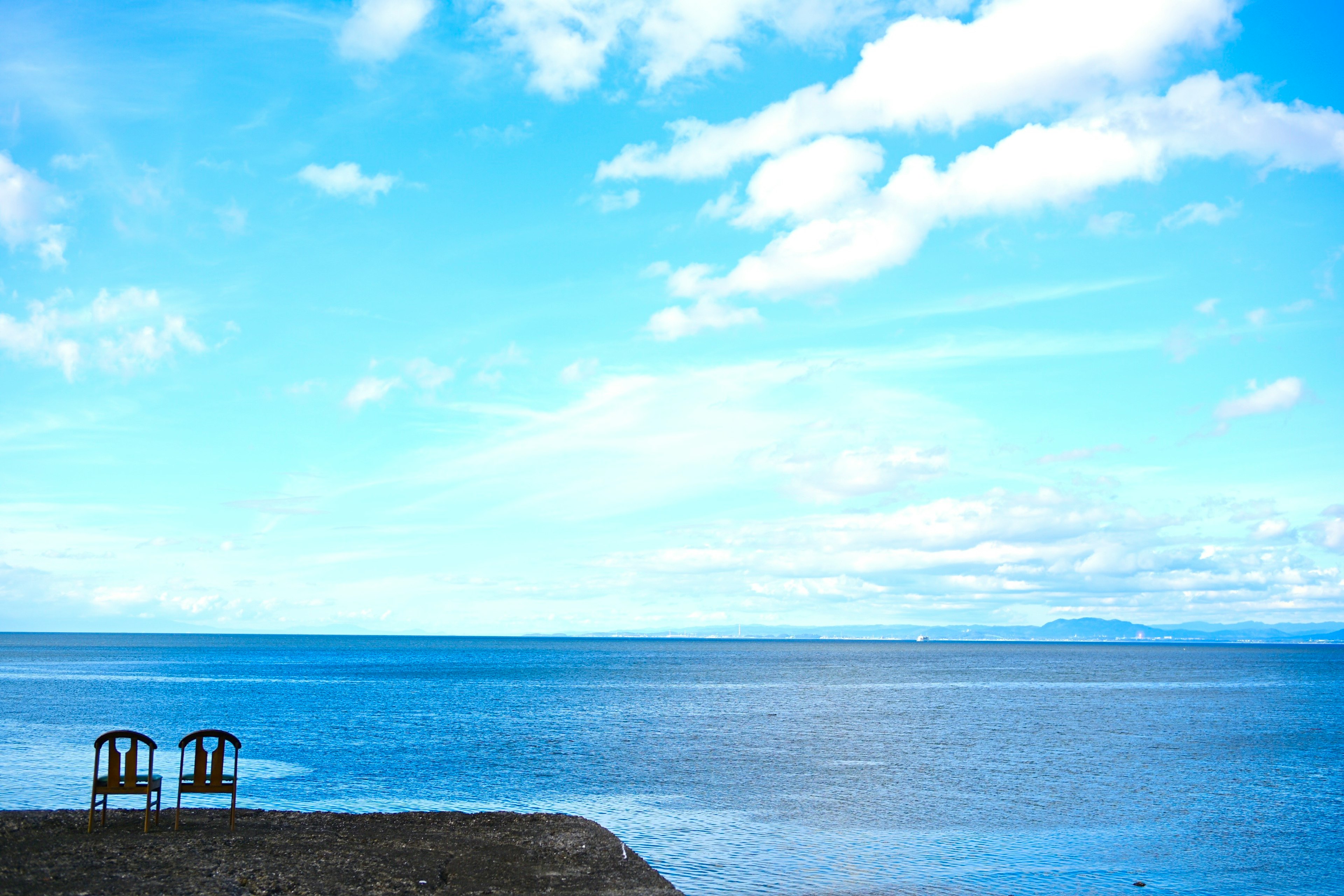 Zwei Stühle mit Blick auf ein weites blaues Meer unter einem hellen Himmel