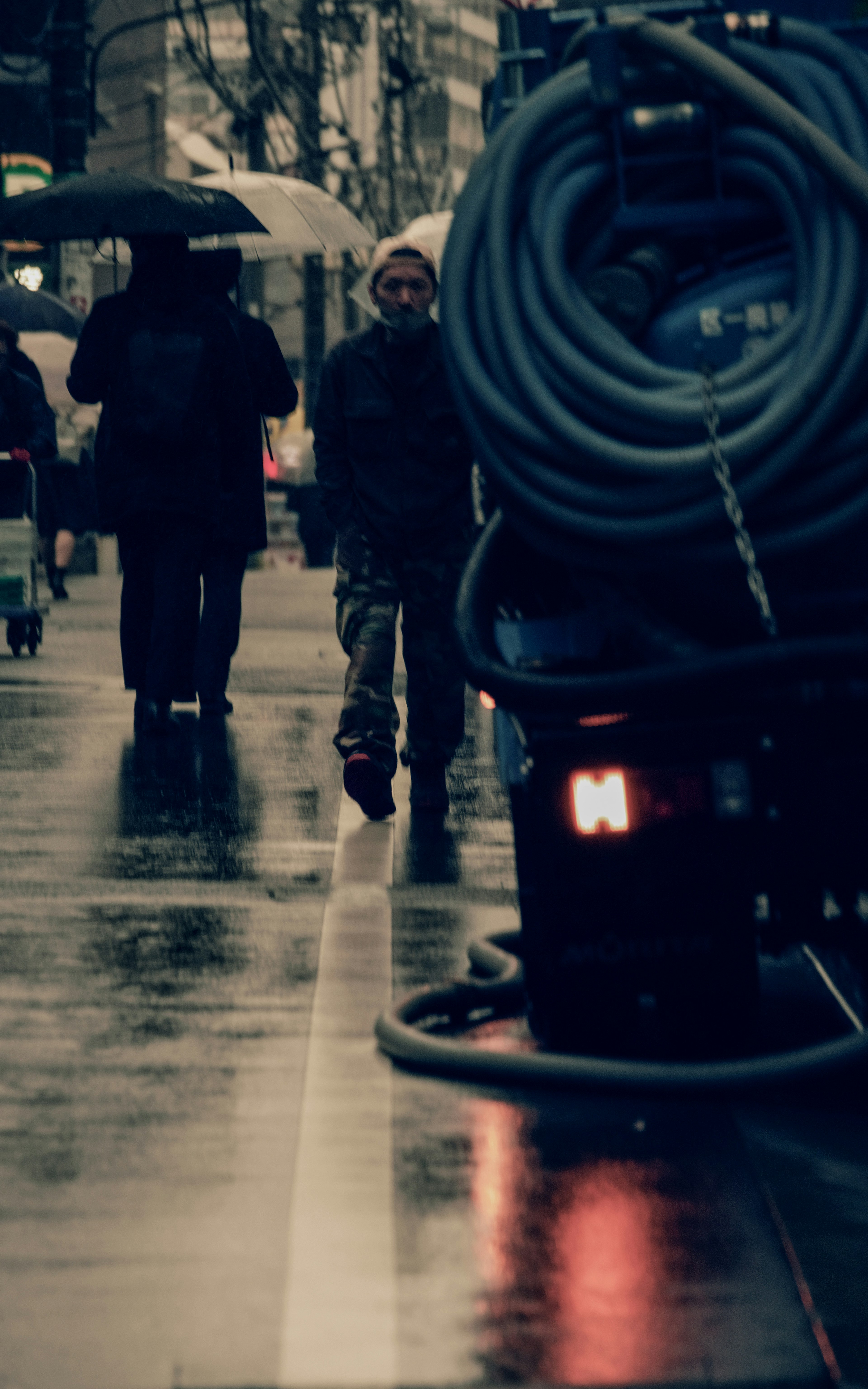 Escena urbana con personas caminando bajo la lluvia y una manguera en el suelo