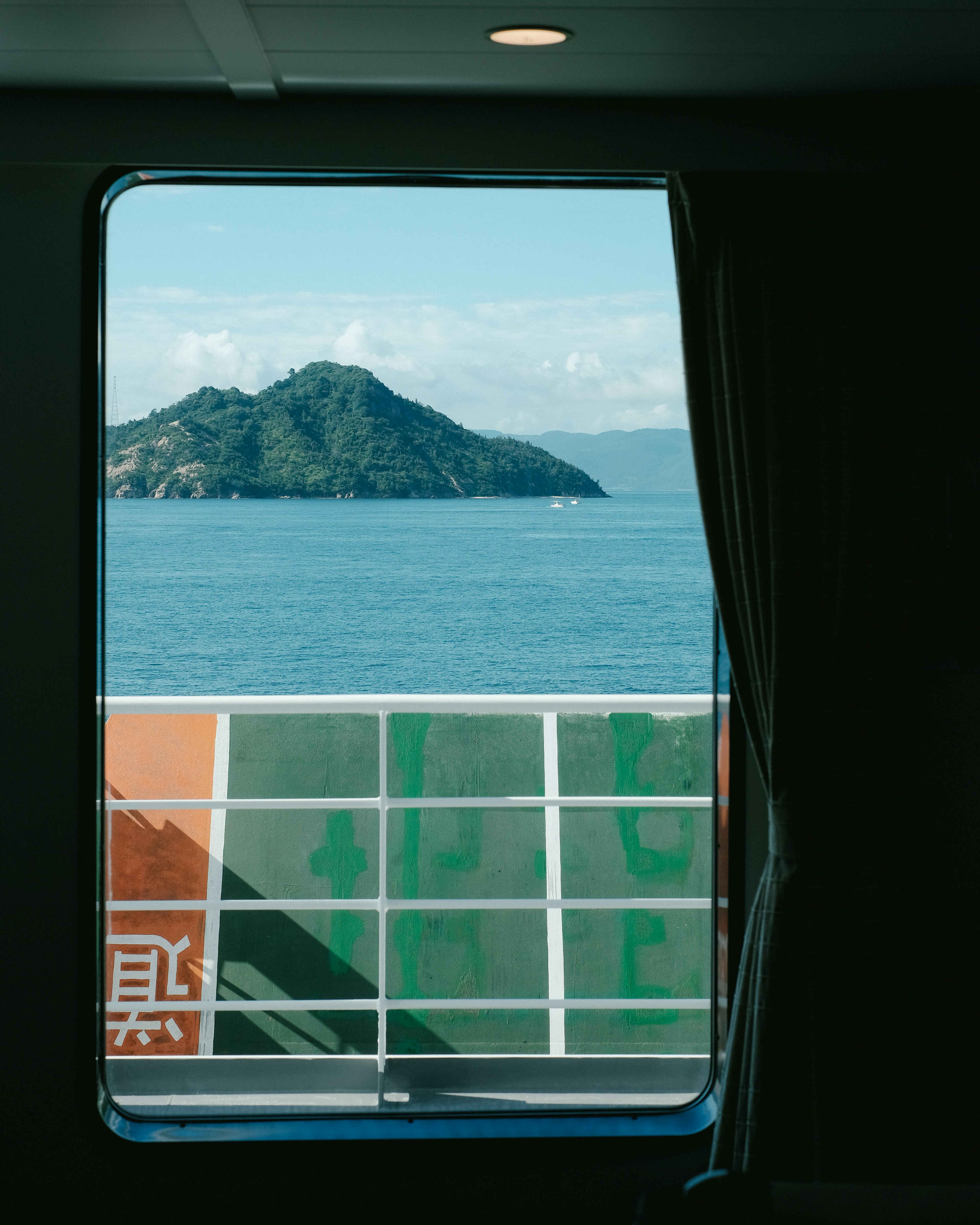 Blick auf das Meer und eine Insel durch ein Fenster, das einen Teil der Seite eines Schiffes zeigt