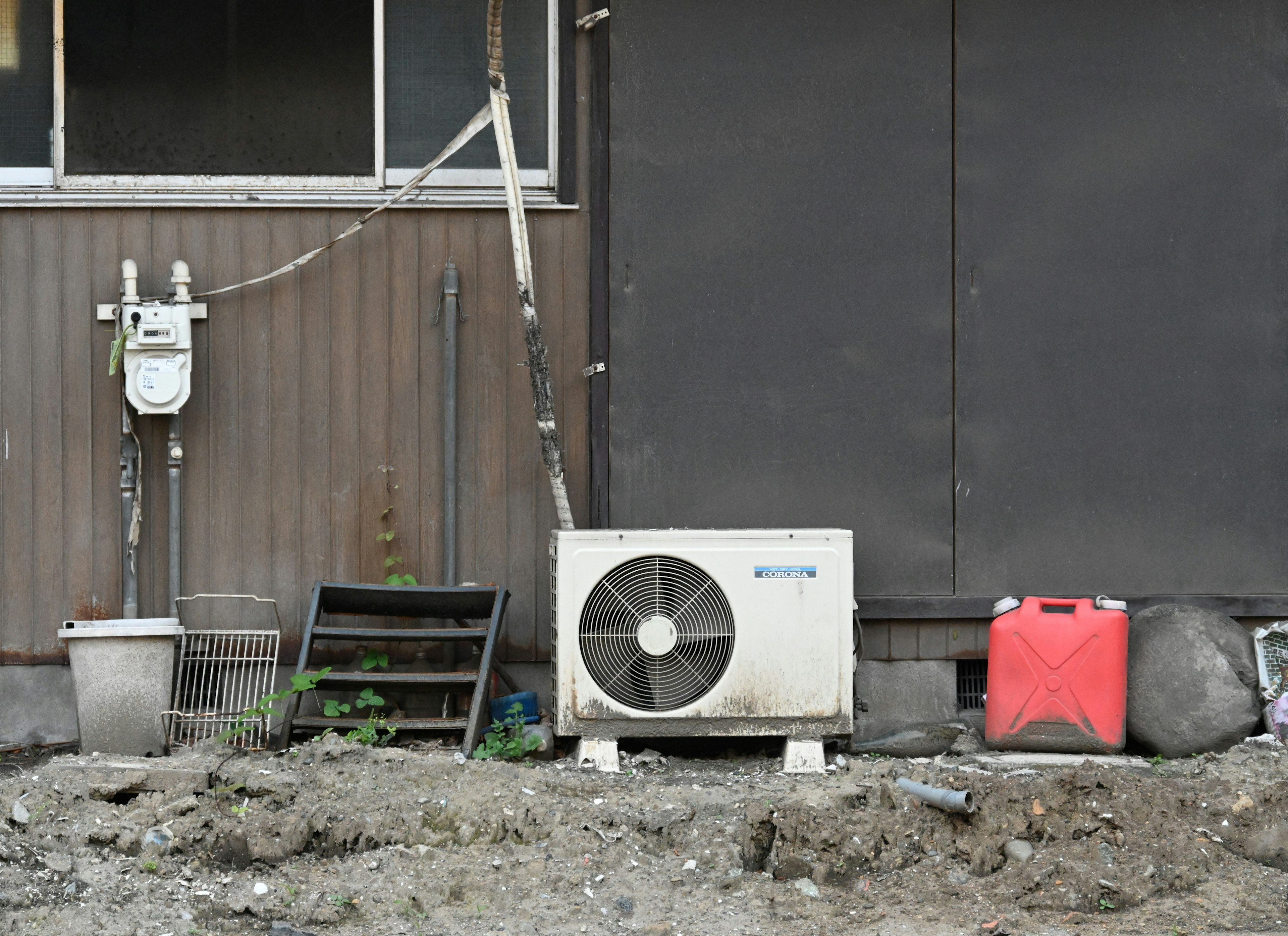 建物の外壁の近くに設置されたエアコンユニットと周囲の雑然とした物品