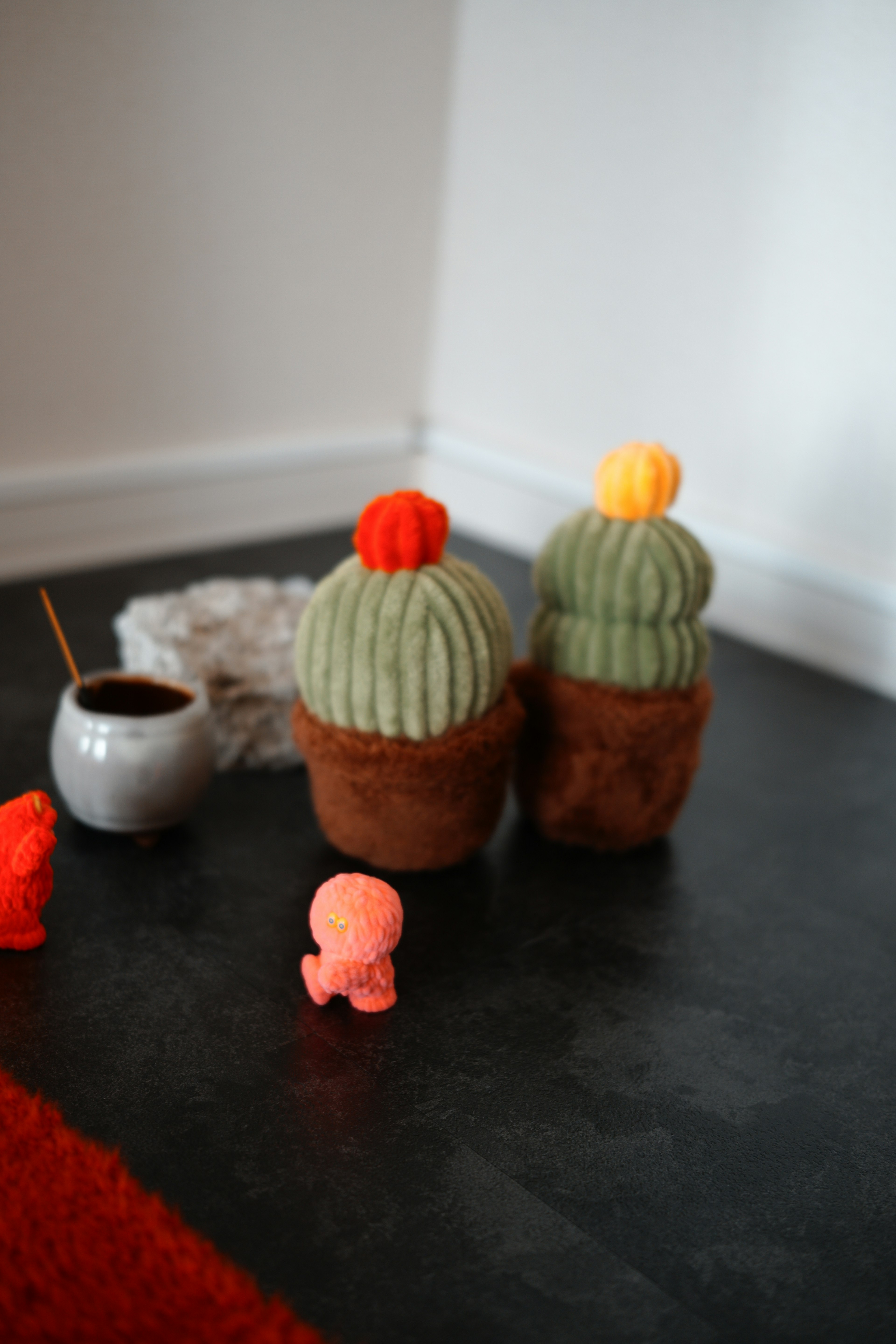 Two knitted cacti with green pom-poms sitting on a dark floor