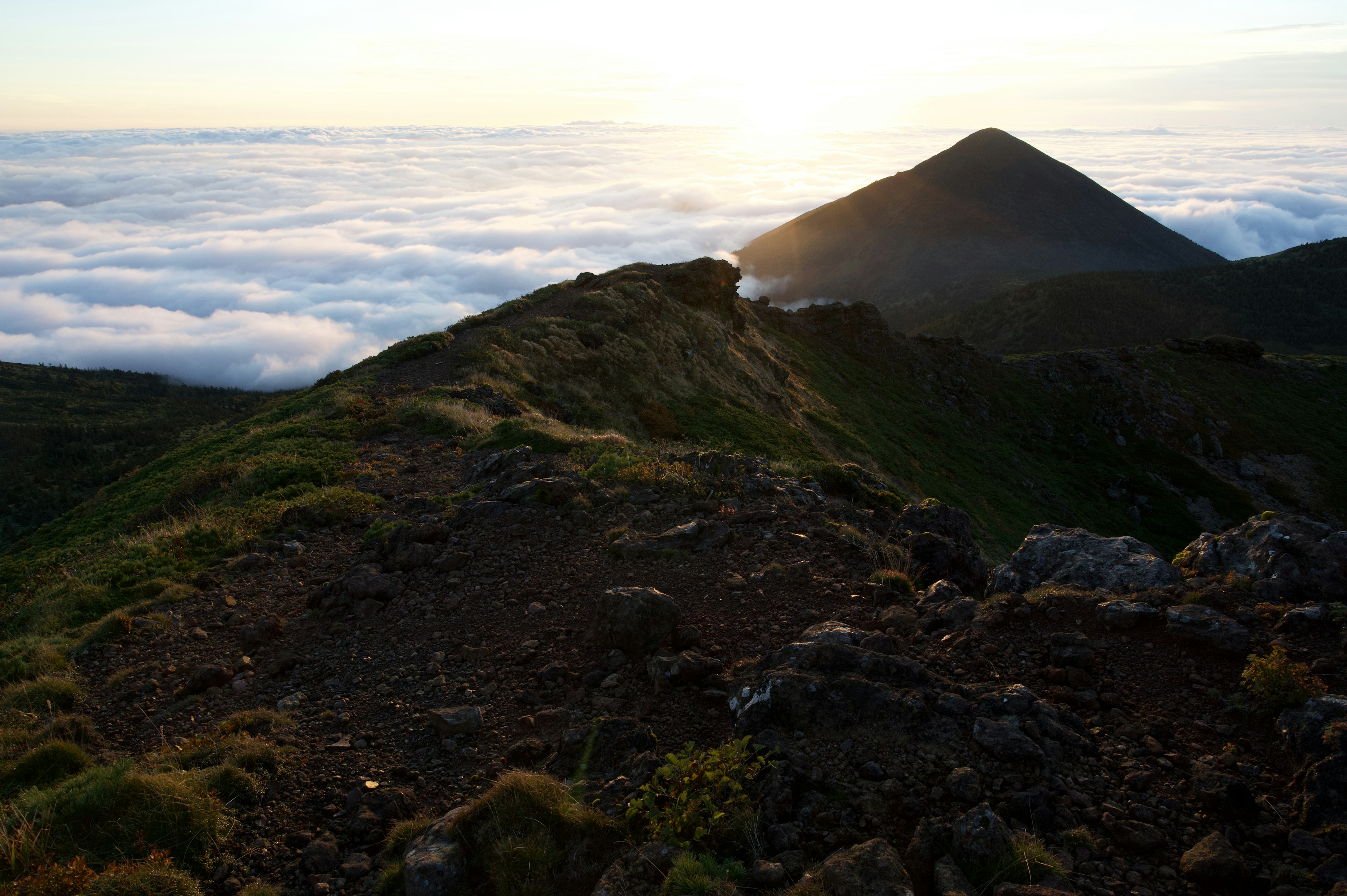 Paisaje montañoso sobre un mar de nubes con el atardecer iluminando la cresta