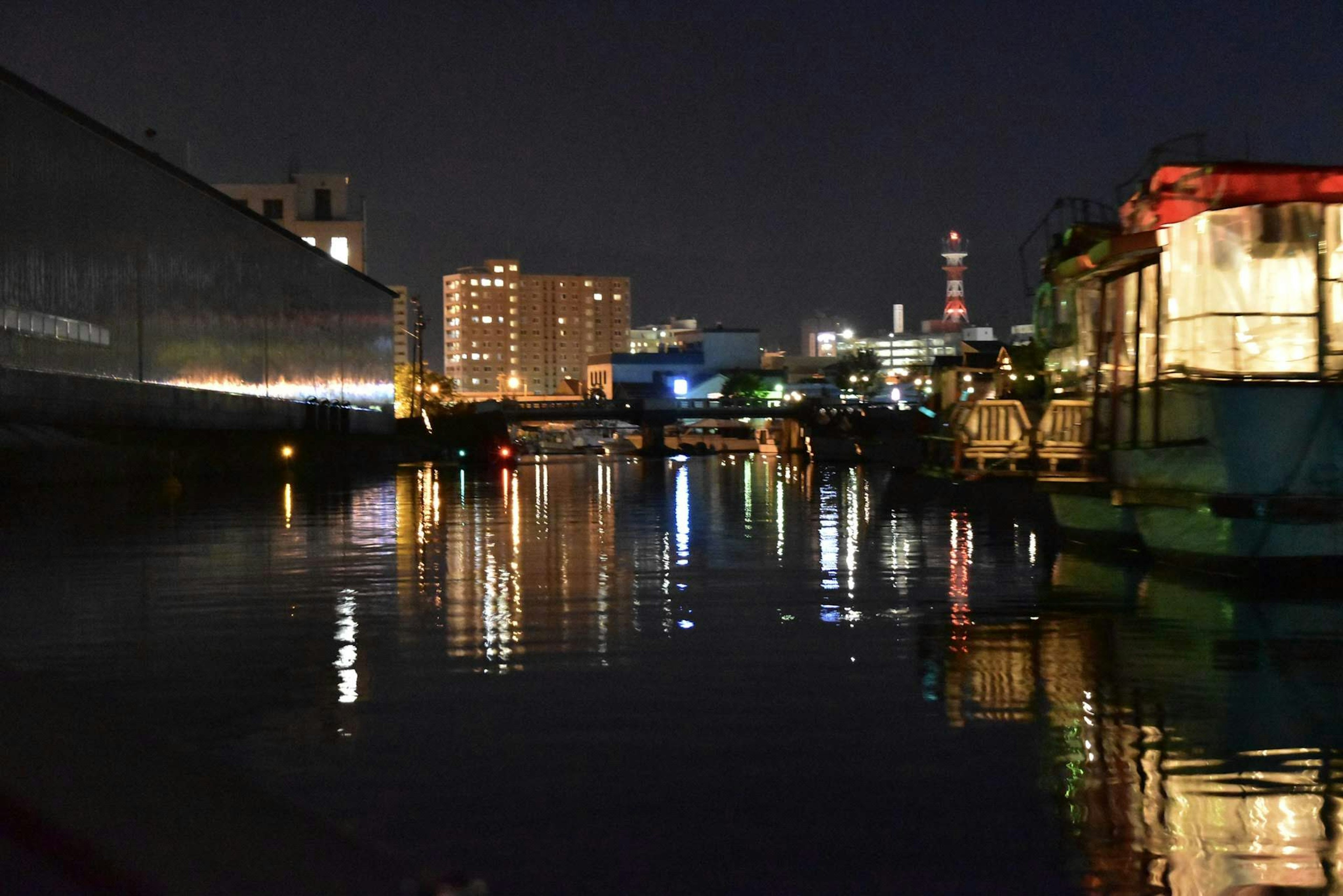 夜の川沿いの風景 高層ビルと反射する光 船が停泊している