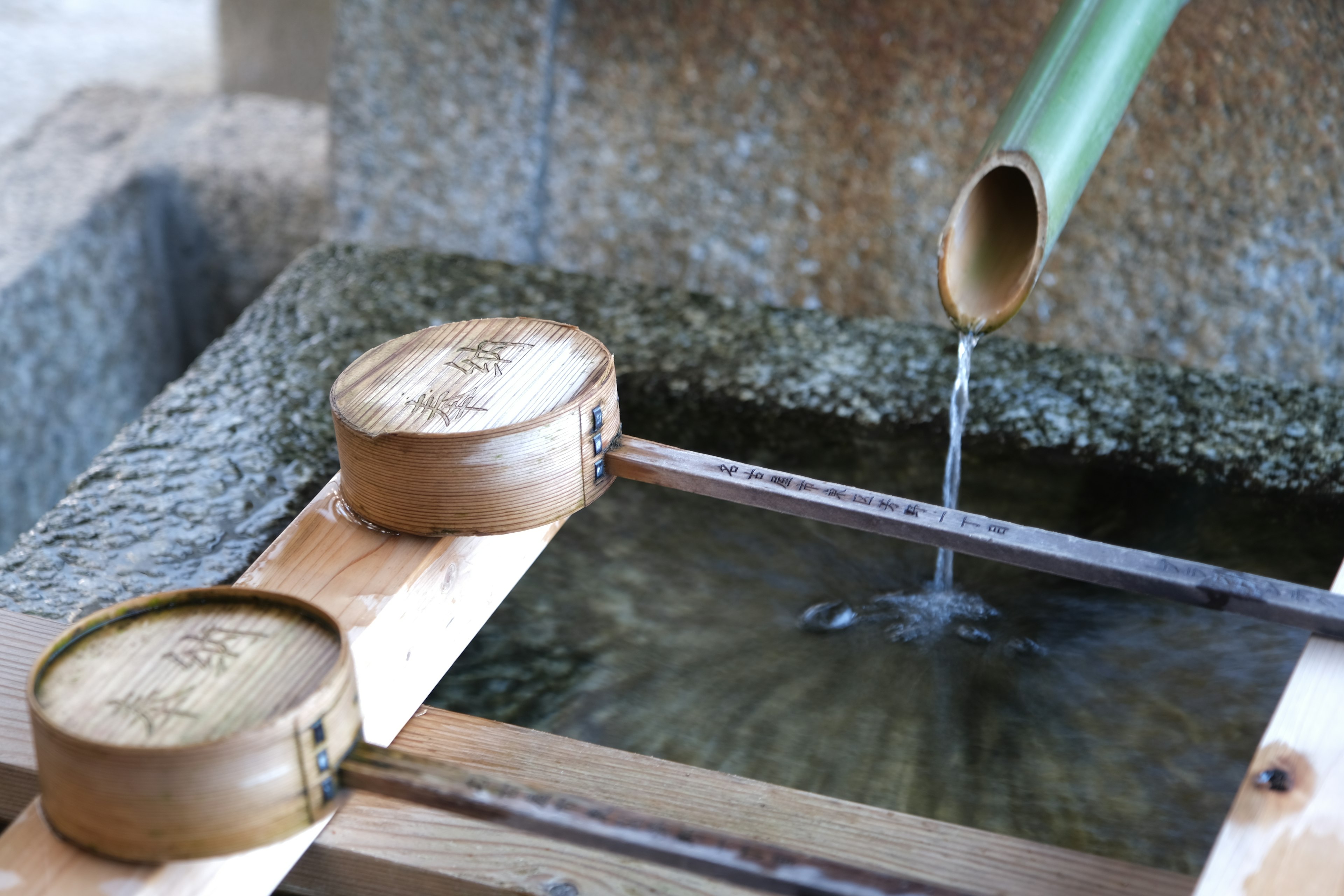 Spout di bambù che versa acqua in un bacino di legno con due contenitori rotondi