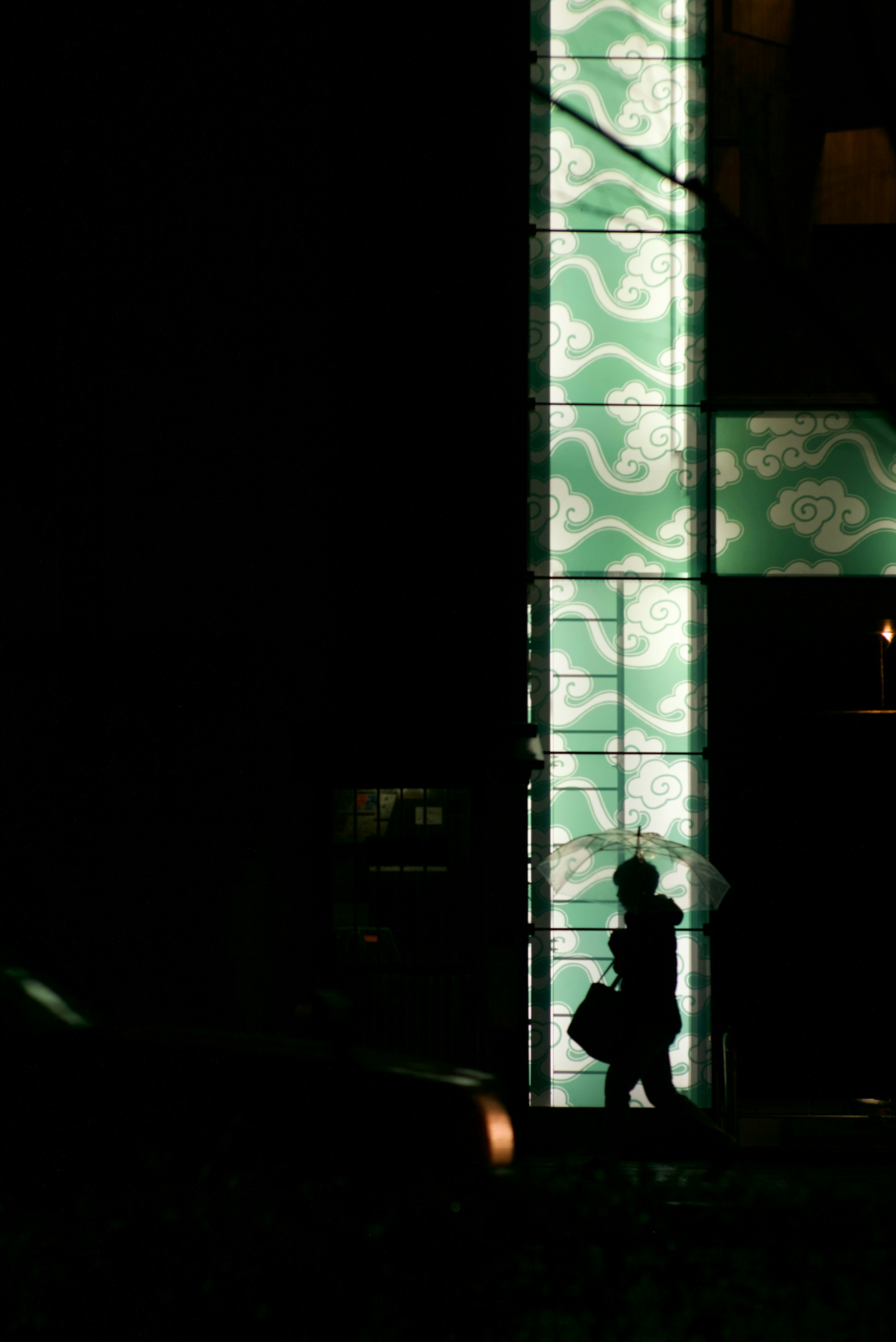 Silhouette di una persona che cammina contro un muro a motivi verdi illuminato in un ambiente scuro