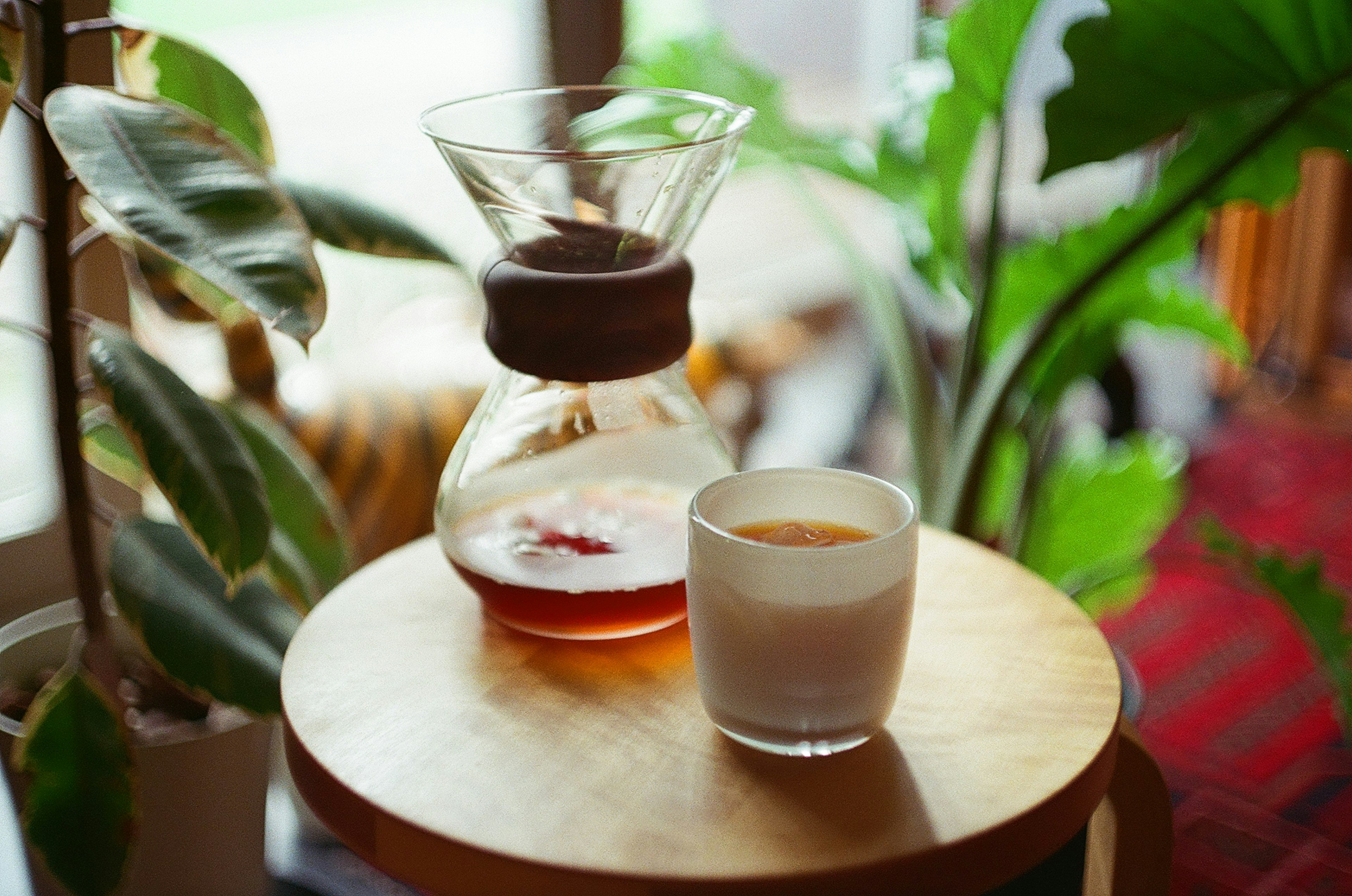 A glass of coffee next to a coffee carafe on a wooden table