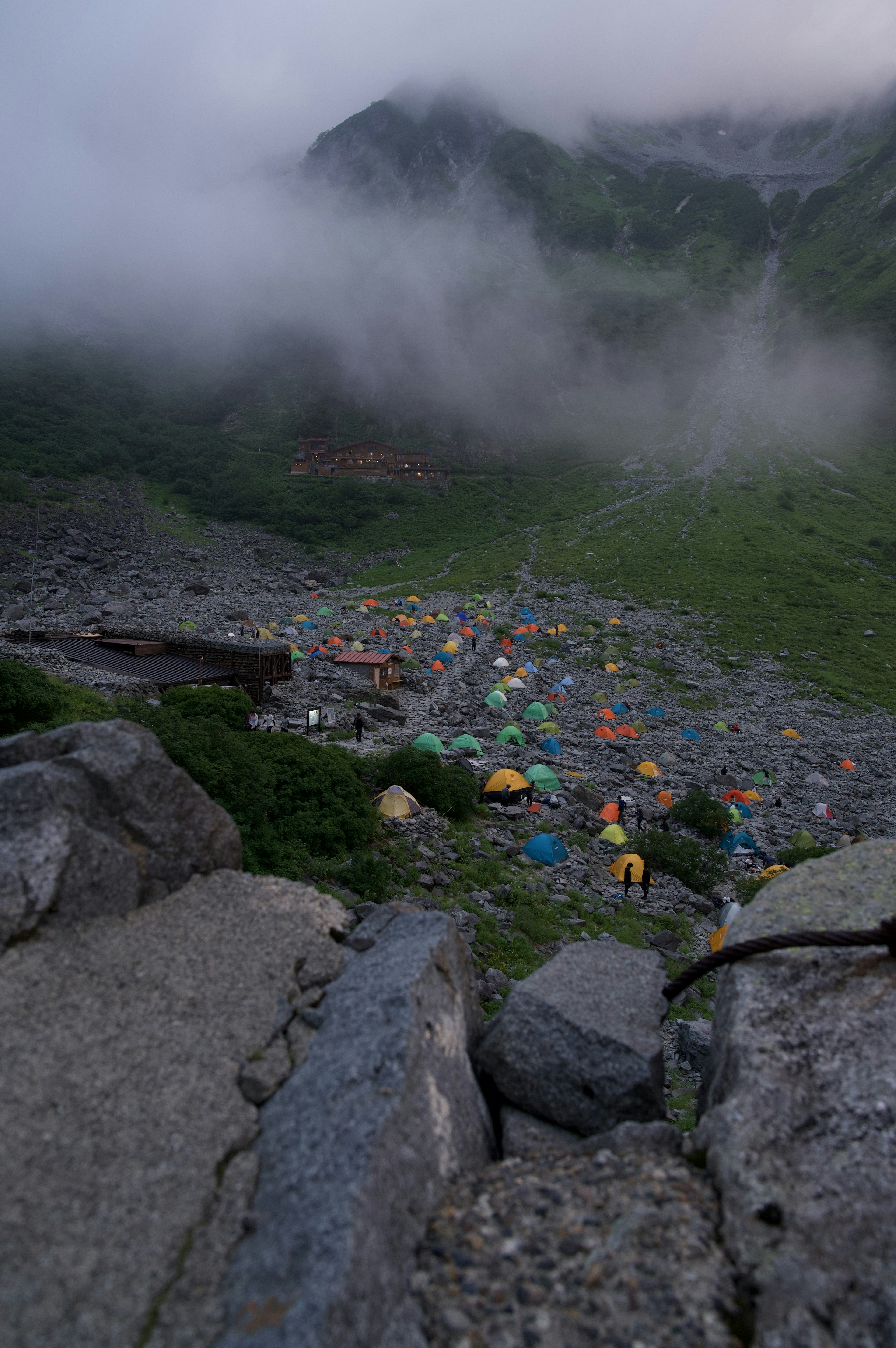 霧の中に隠れた色とりどりのテントが並ぶ山の風景