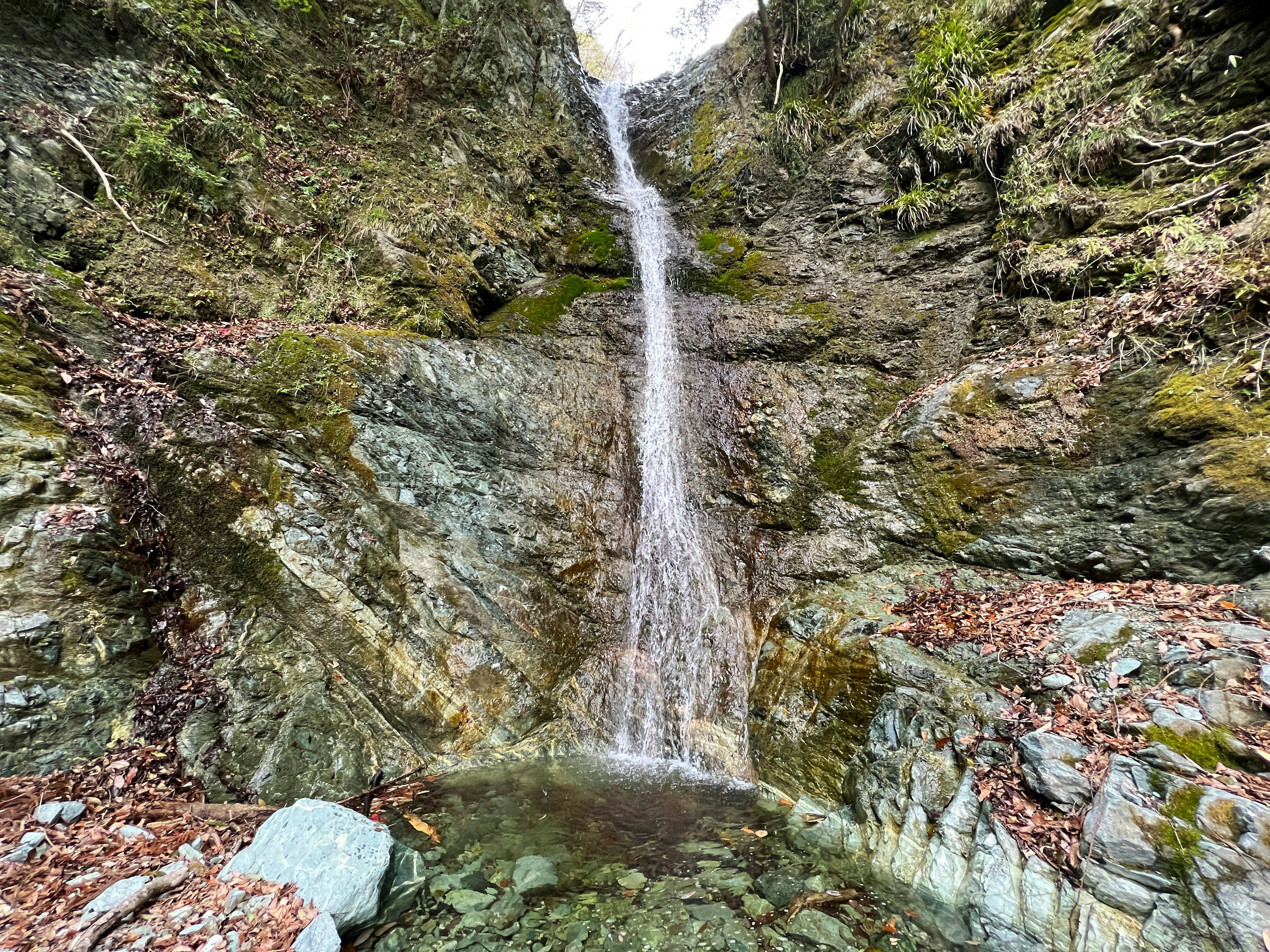 Sebuah air terjun yang indah mengalir di antara batu-batu dikelilingi oleh vegetasi hijau yang subur dalam pemandangan alami