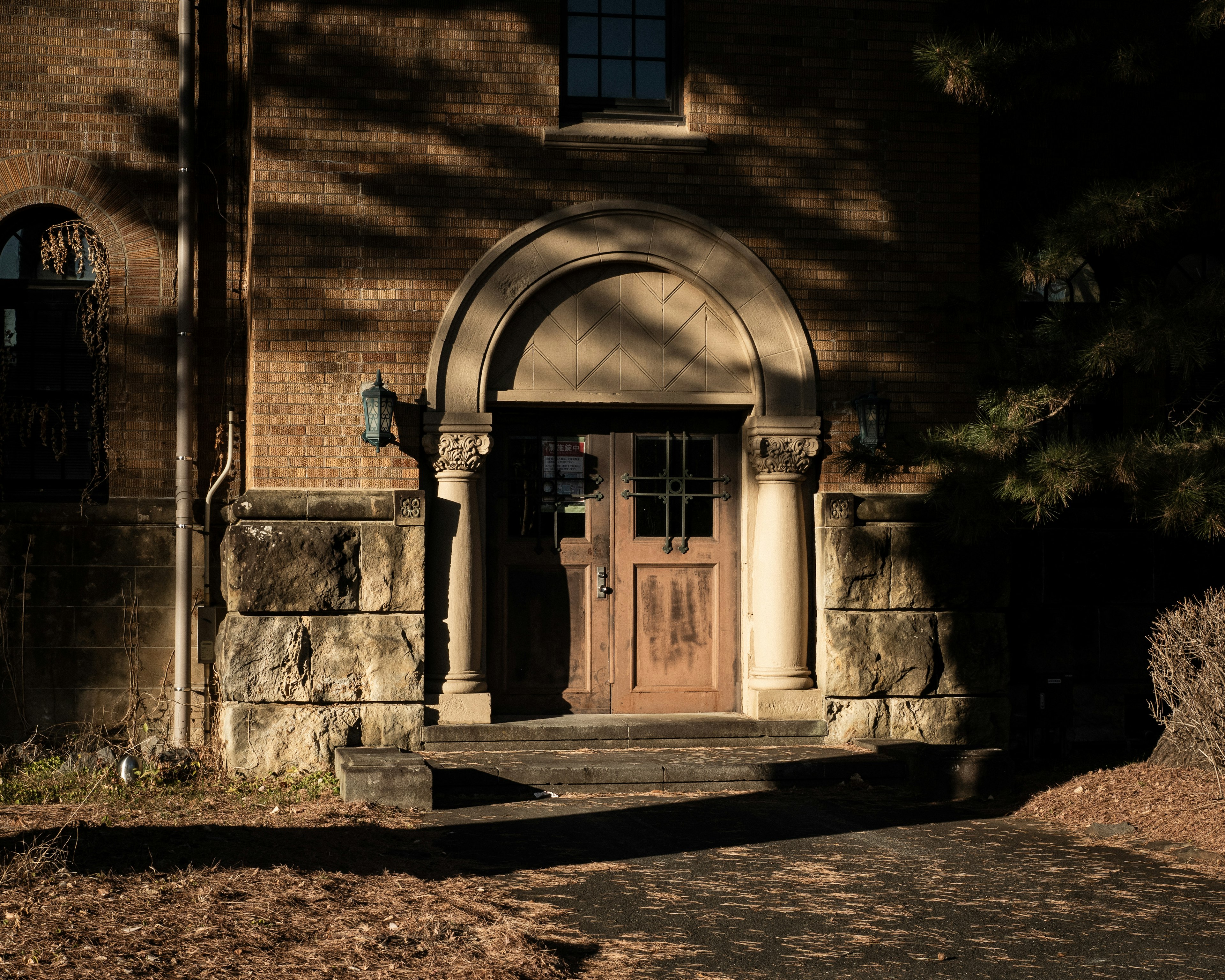 Entrance of an old brick building with an arched doorway and wooden door surrounded by shadows