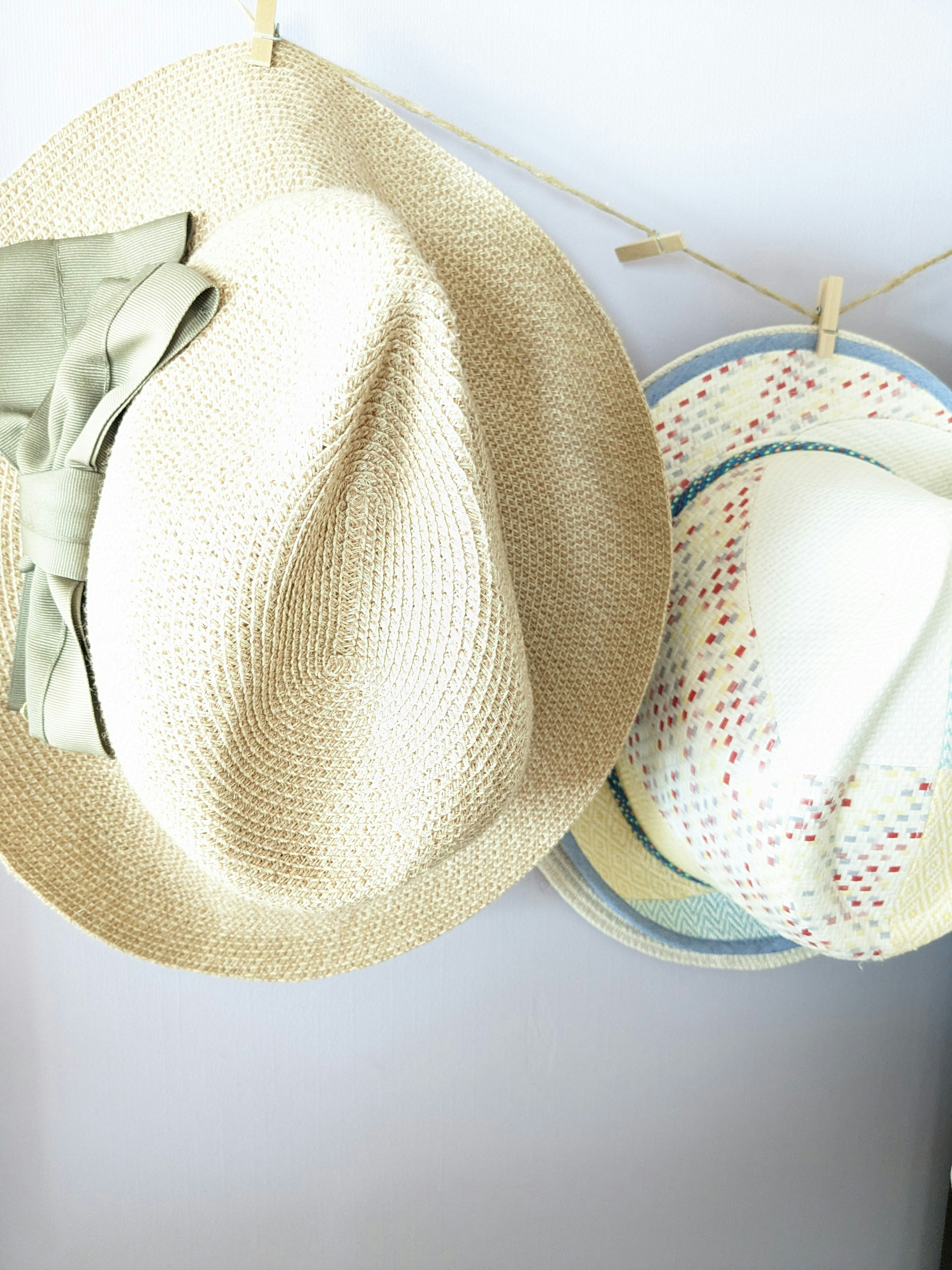 Dua topi menggantung di dinding satu topi jerami dengan pita hijau dan satu topi putih bermotif