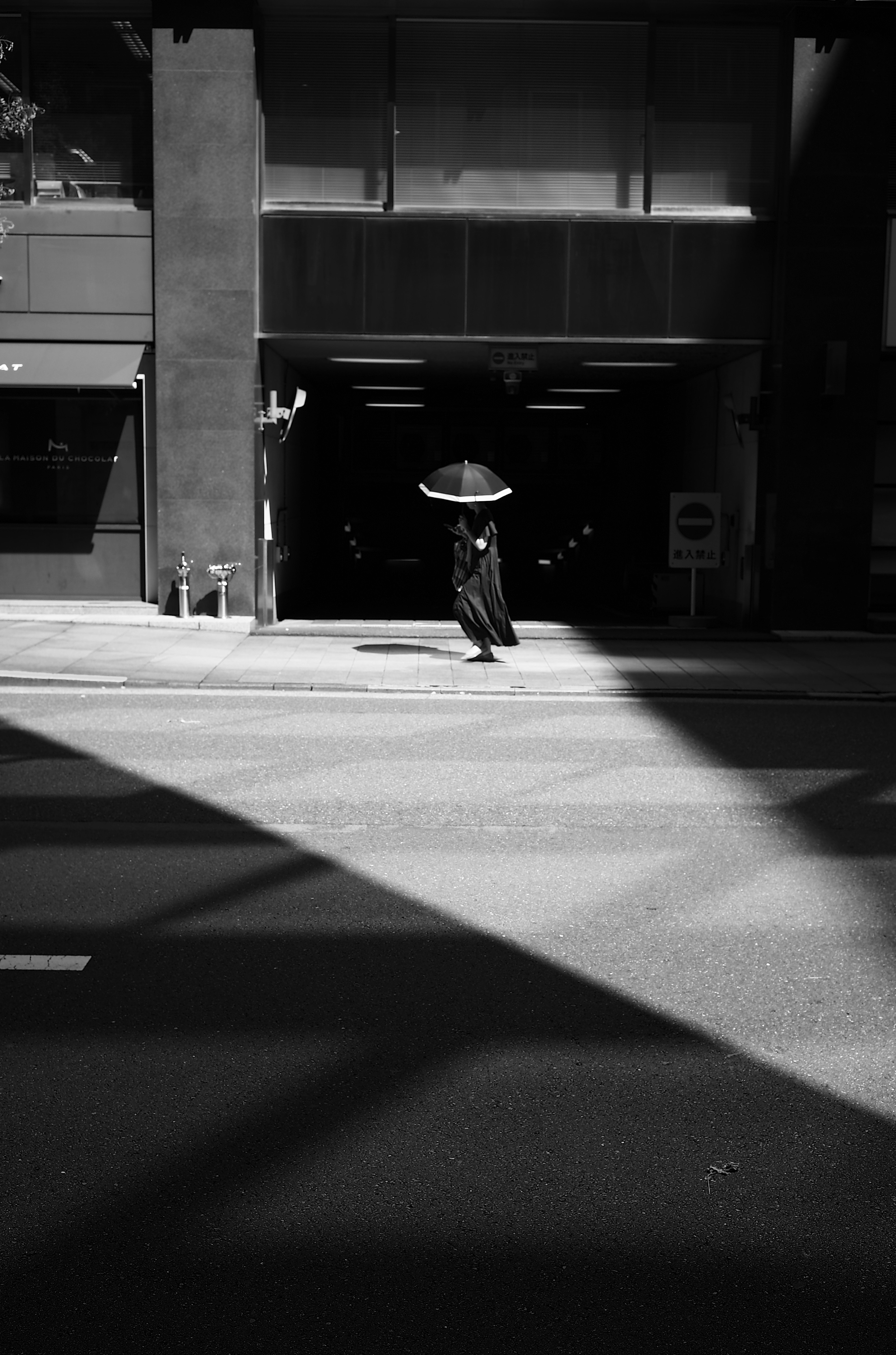 Une personne tenant un parapluie traversant une rue en contraste noir et blanc