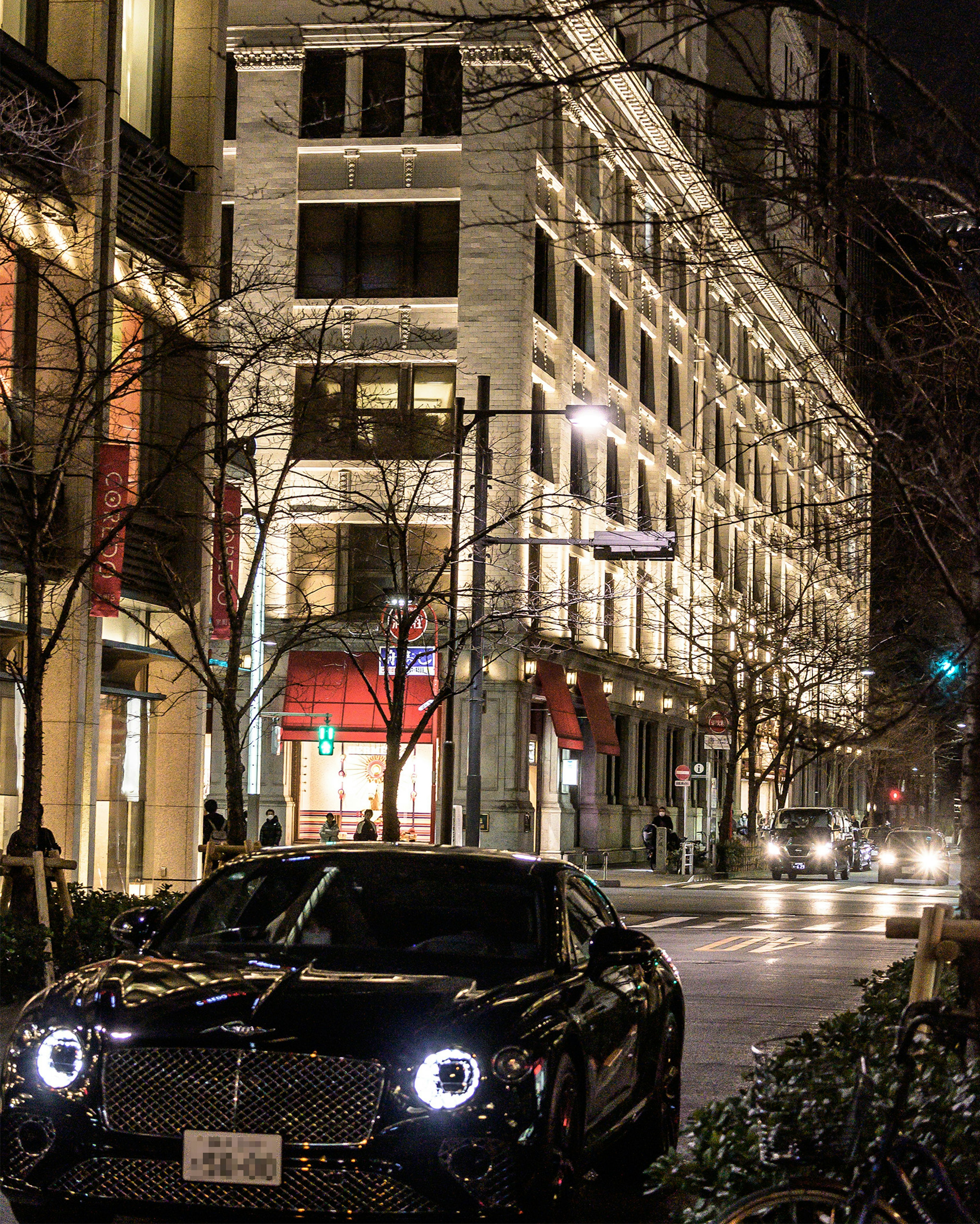 Sebuah Bentley hitam diparkir di jalan kota di malam hari dengan gedung yang diterangi