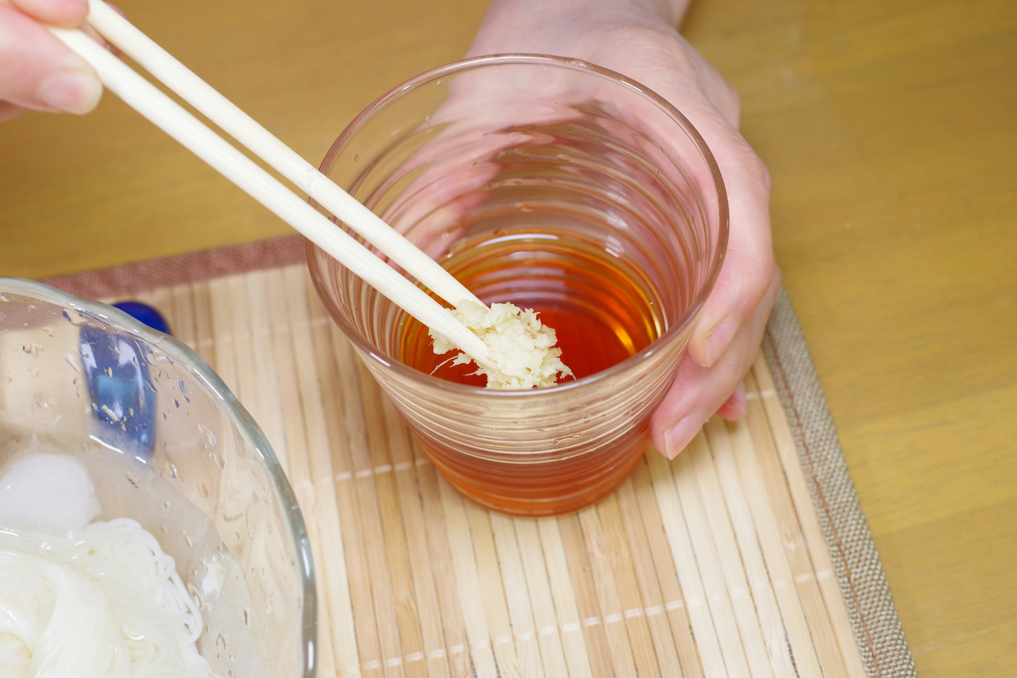 A hand holding chopsticks dipping something into a transparent cup filled with a red liquid