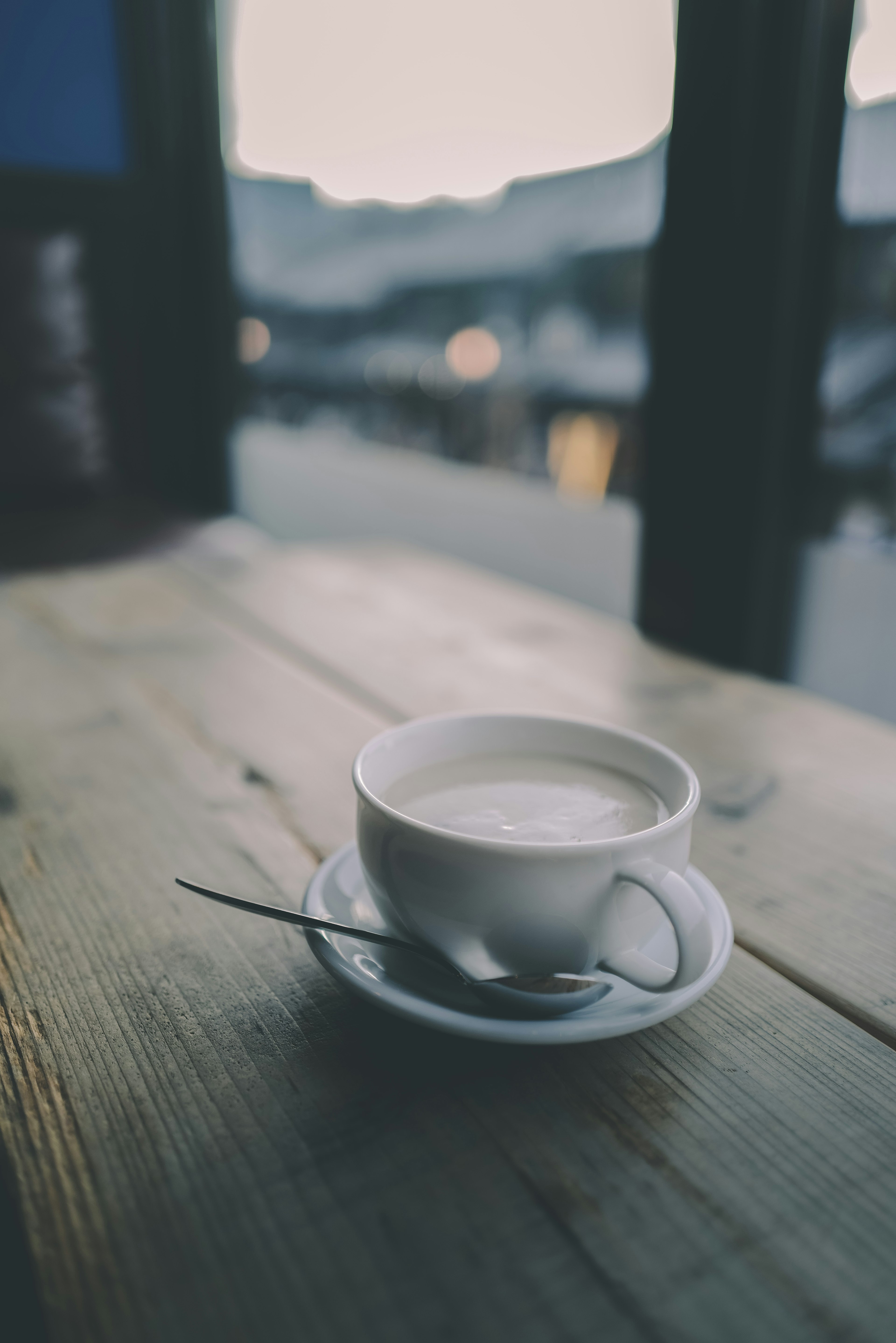 木製のテーブルの上に置かれた白いカップのコーヒー　背景にはぼんやりとした風景