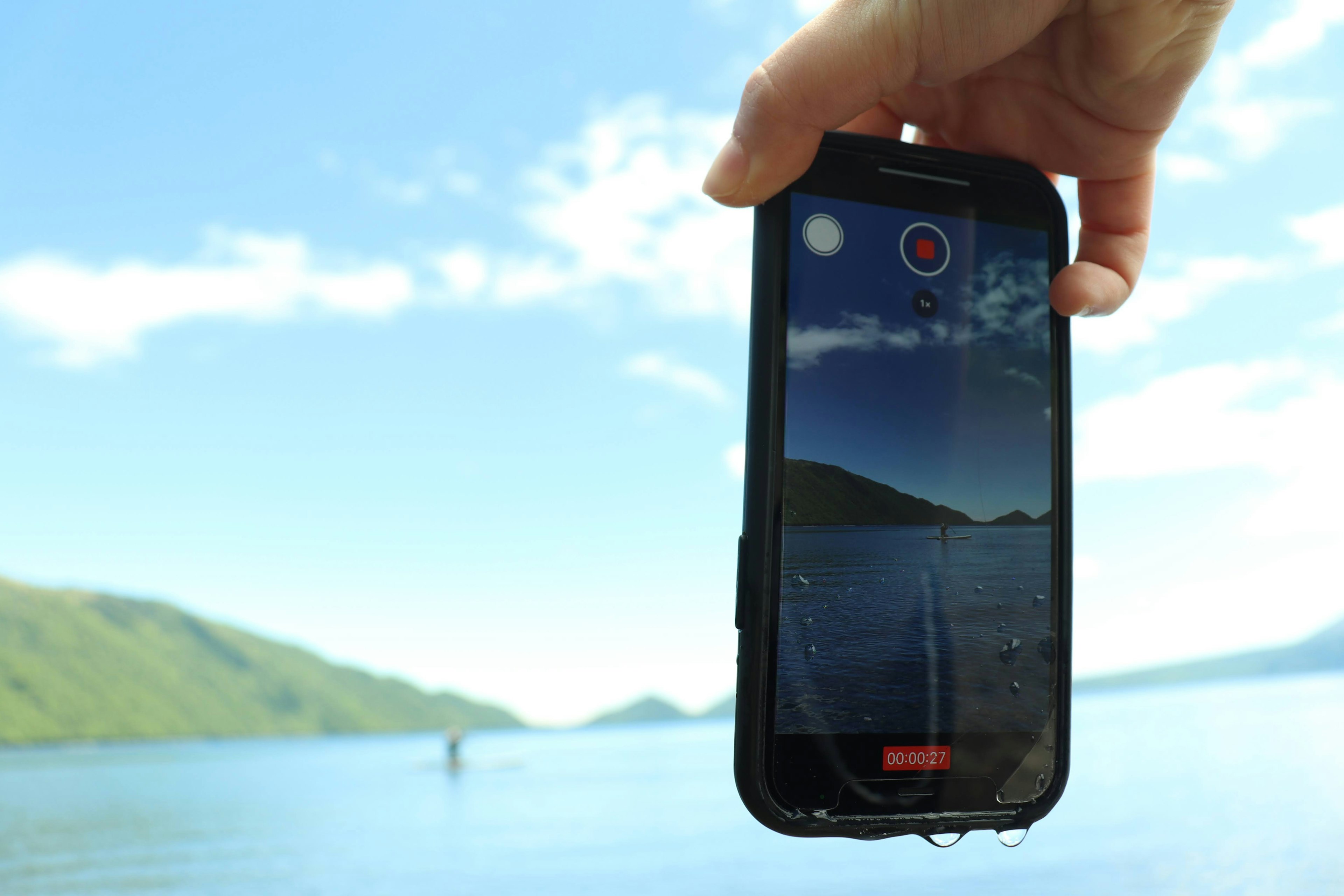 A smartphone held in hand displaying a scenic lake view