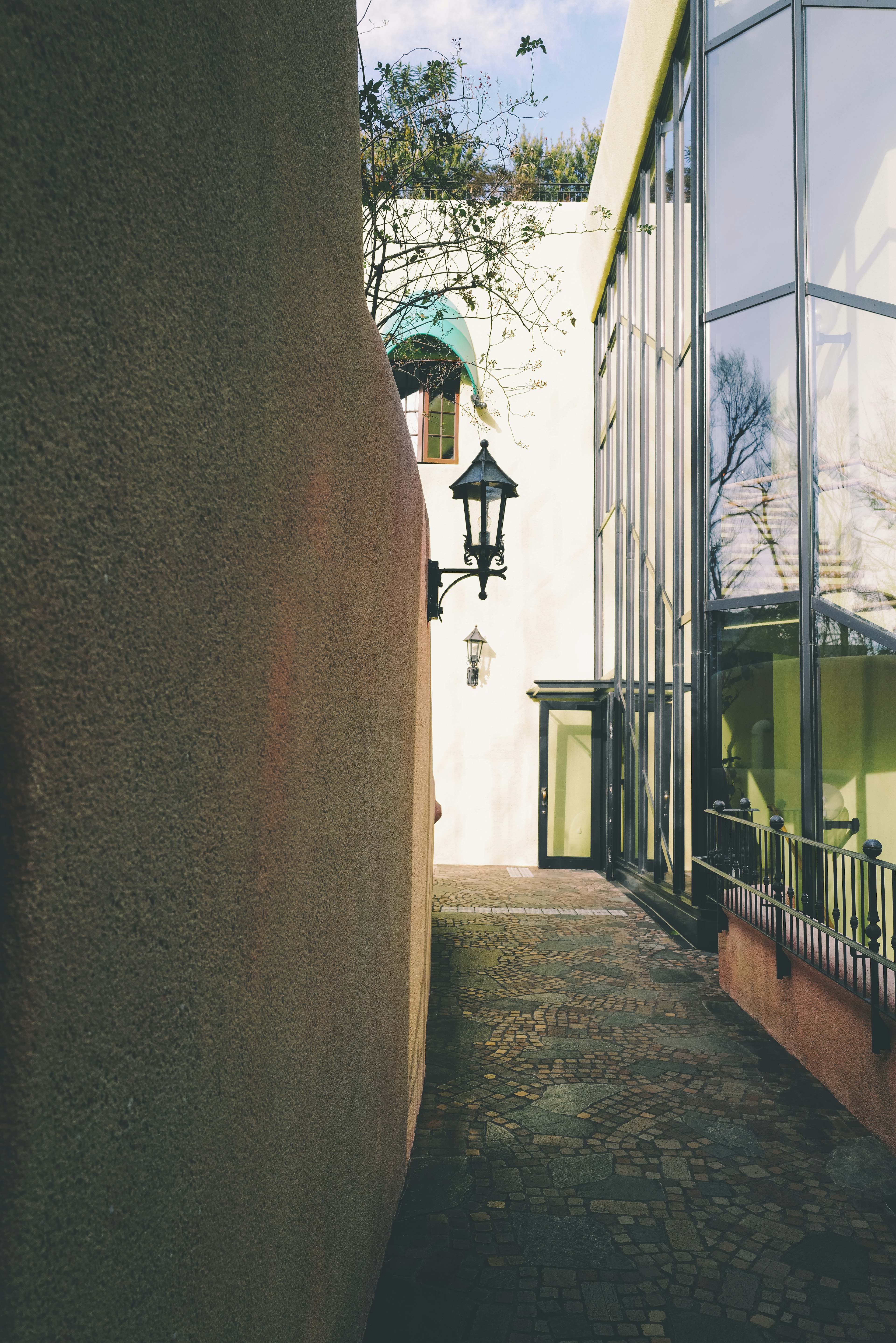 Narrow passageway flanked by a glass building and a wall