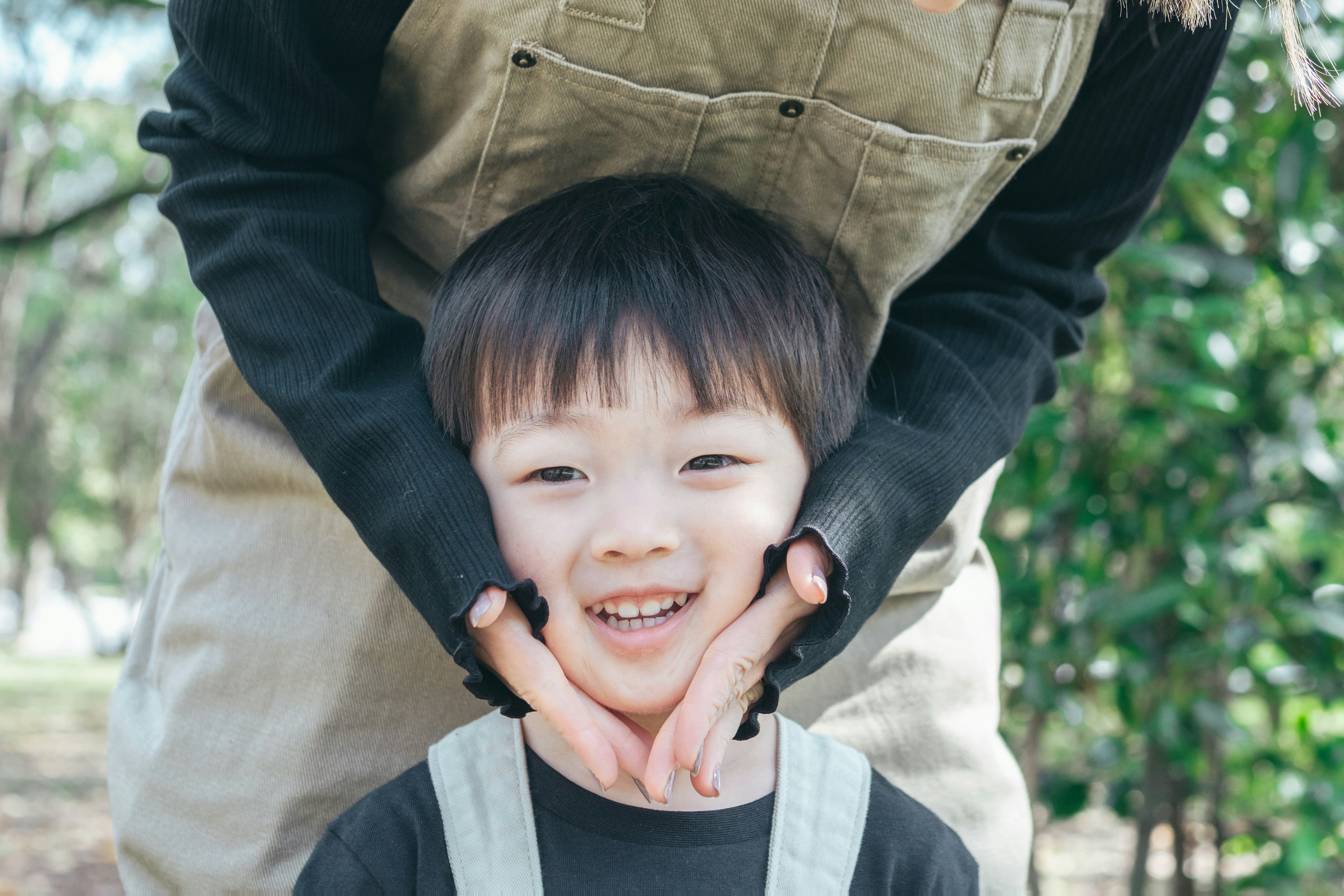 Un enfant souriant avec les mains sur son visage soutenu par un parent