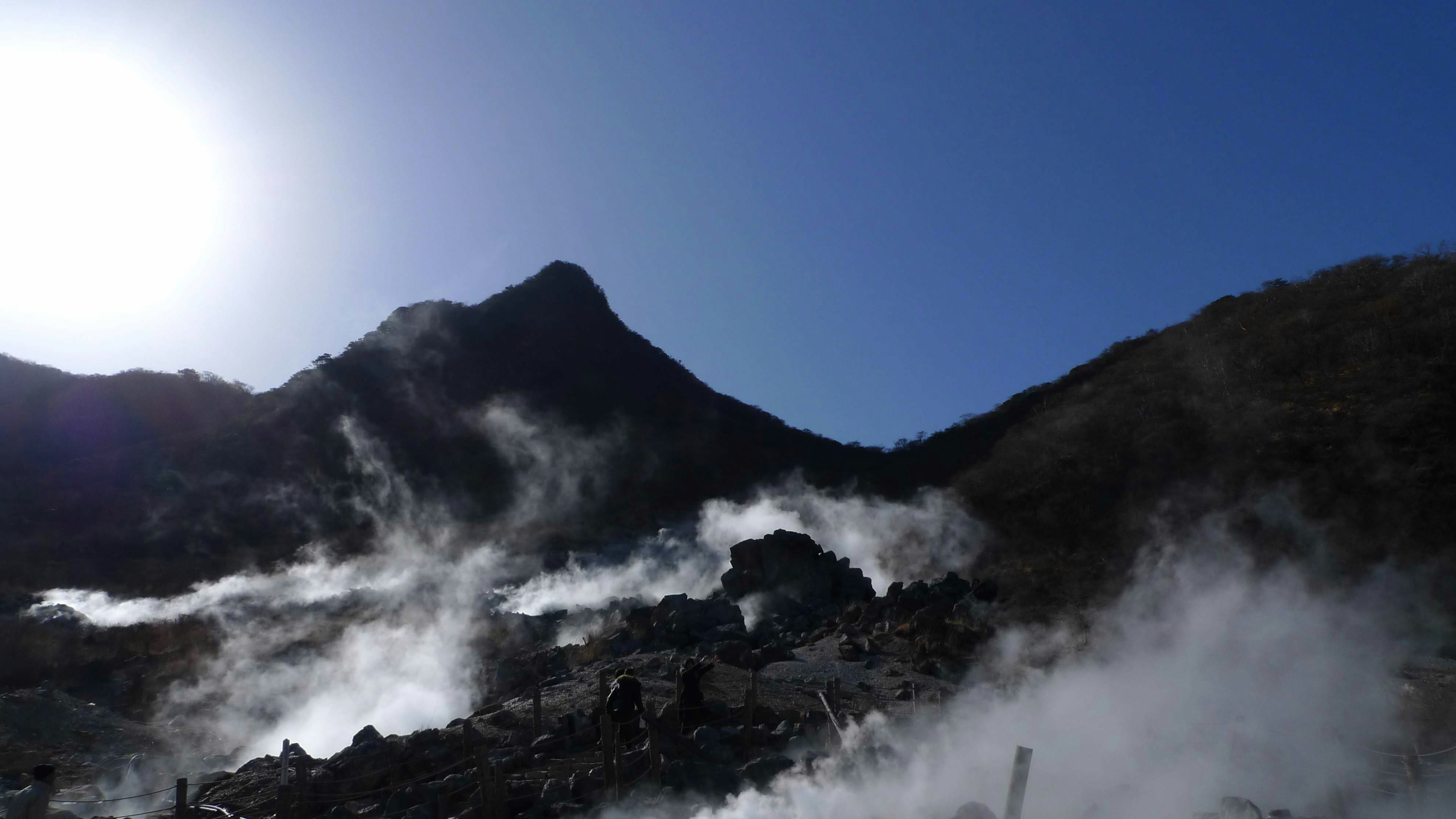 Mountain landscape with rising steam, blue sky, sun, signs of volcanic activity