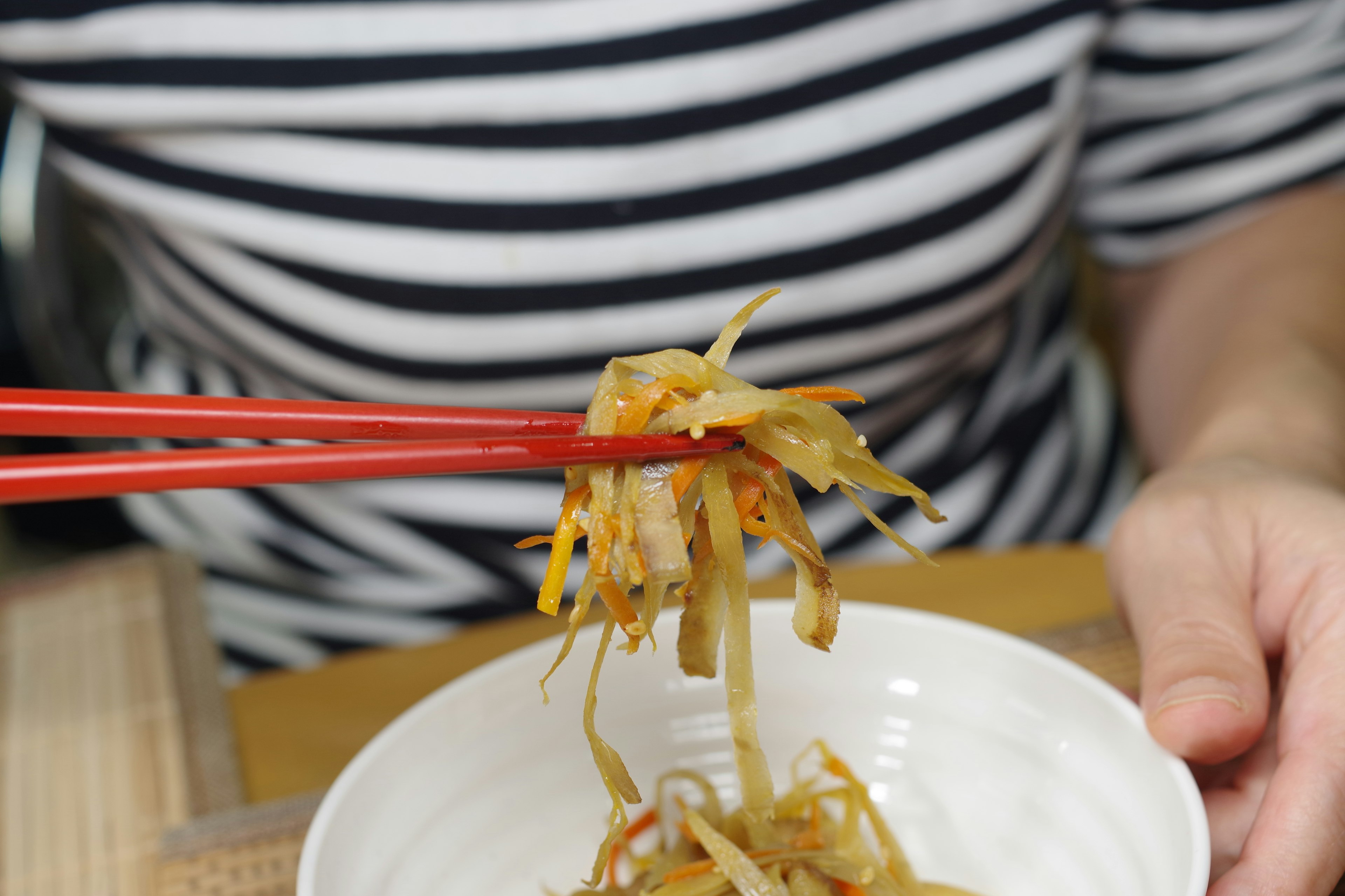 Person wearing a striped shirt picking up vegetables with chopsticks