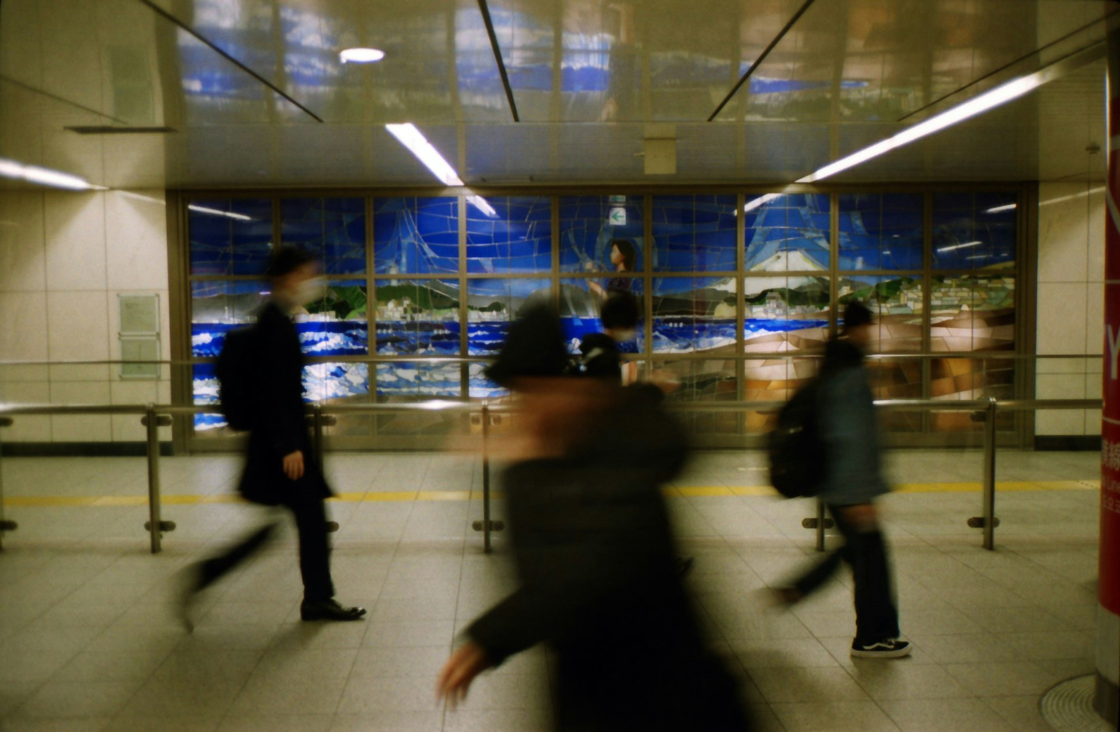 人々が動いている地下鉄の駅の風景 背景に青いアートがある