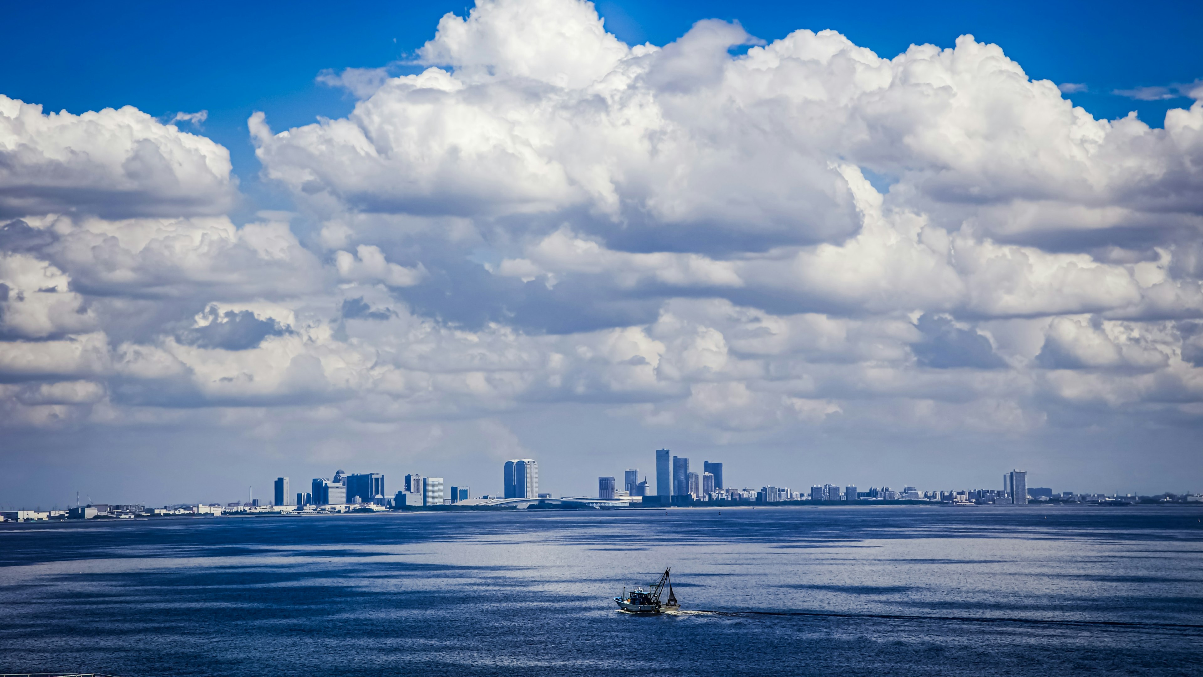 Silhouette della città contro un cielo blu e nuvole bianche con una piccola barca sull'acqua